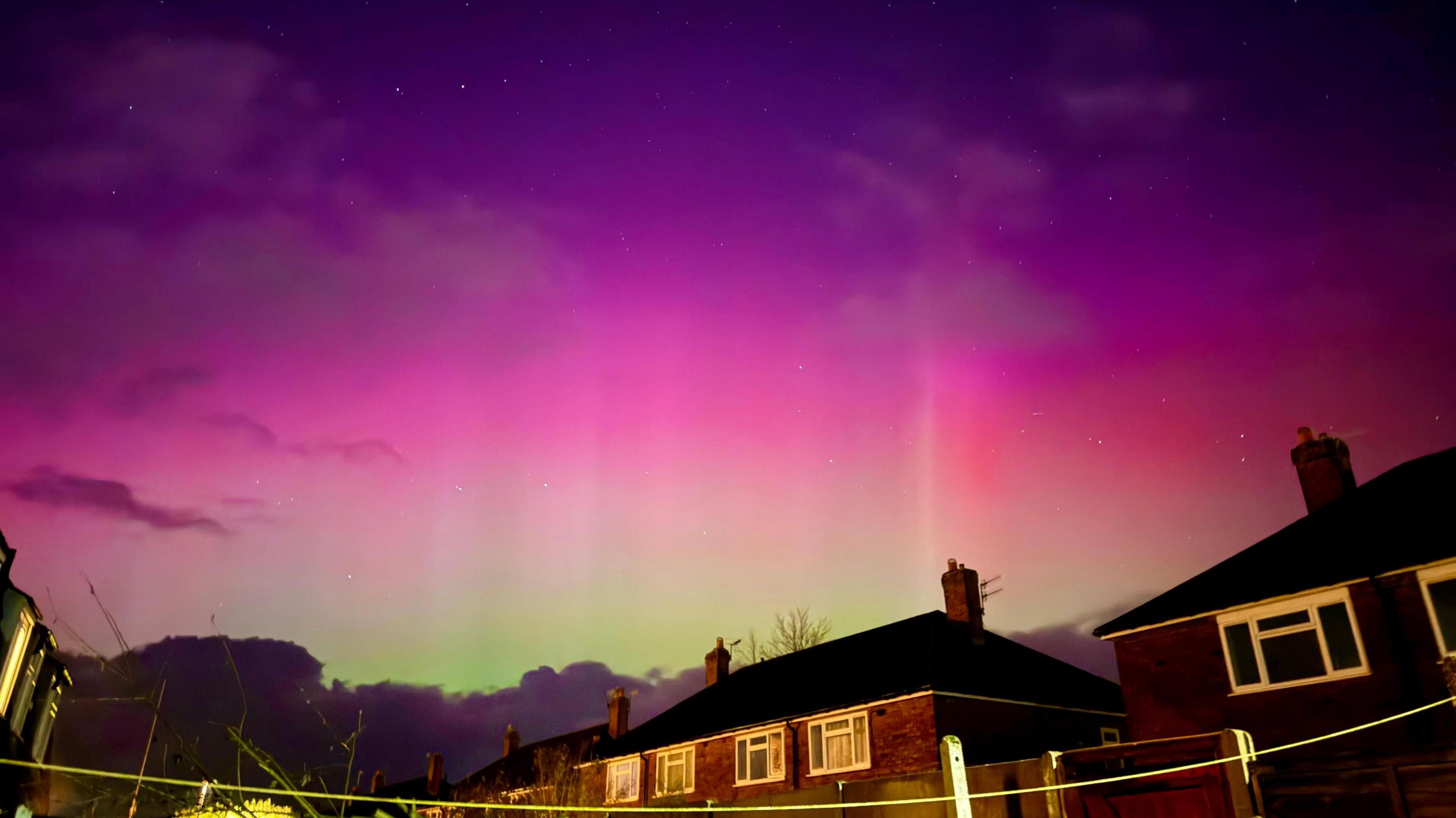 reds and purple colours of the aurora with a tinge of green above houses