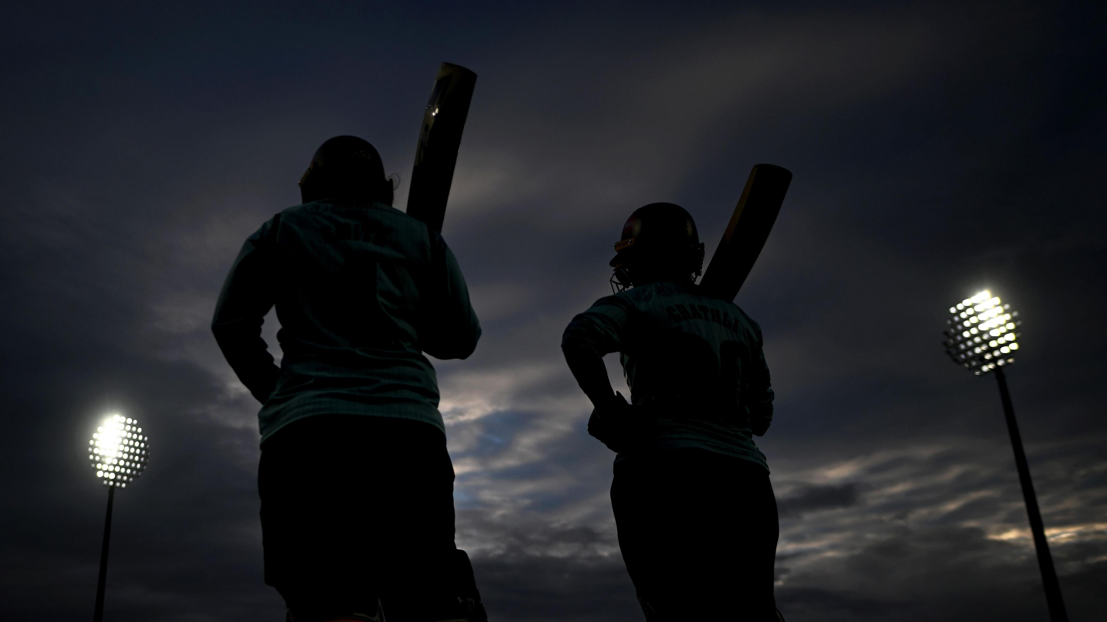 Two players are silhouetted against the dark sky and floodlights as they walk out to bat in the T20 women's cup final at Taunton