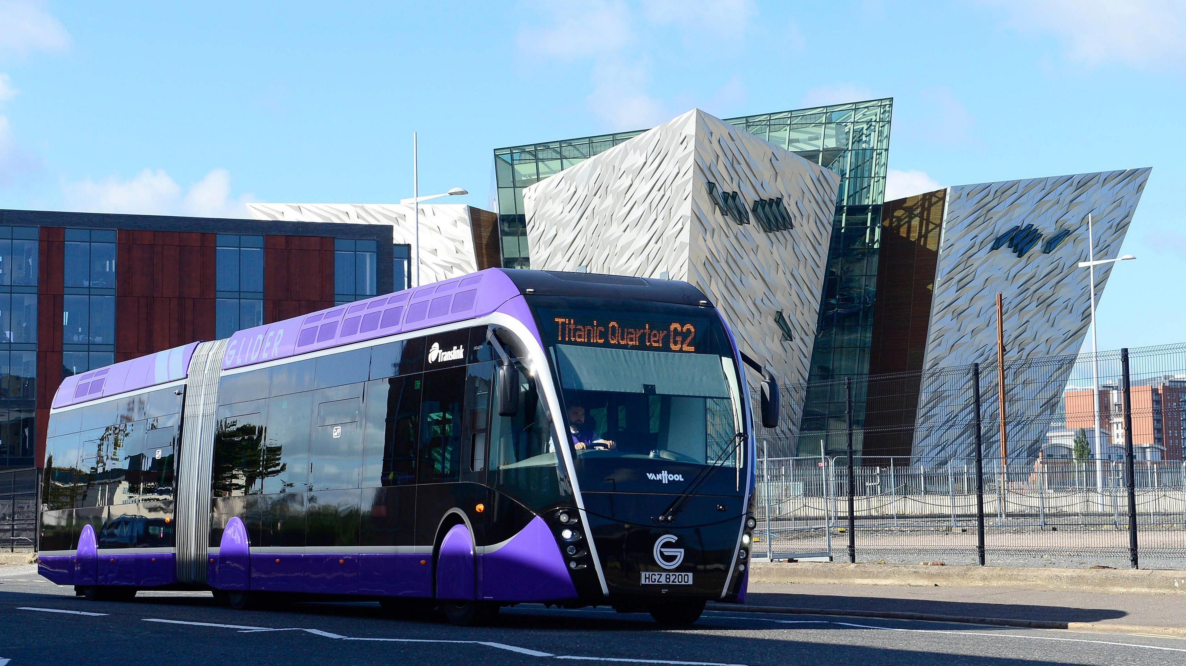 A wide-shot of the purple Glider bus with the Titanic museum building in the background.