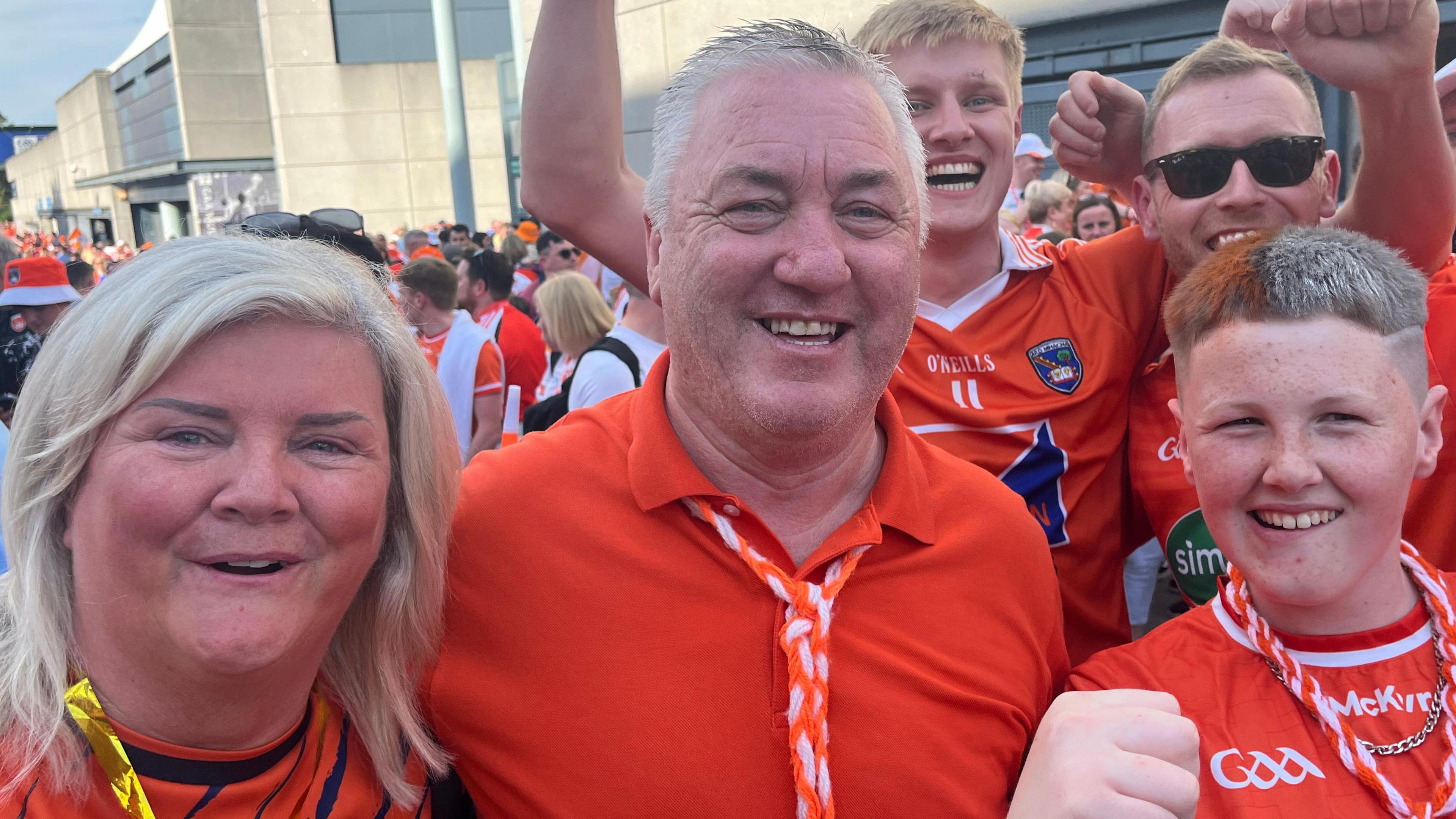 A group in orange celebrating the win. There's a woman with shoulder length blonde hair, a man with grey hair, ad a boy with orange and white in his hair. People are cheering in the background.