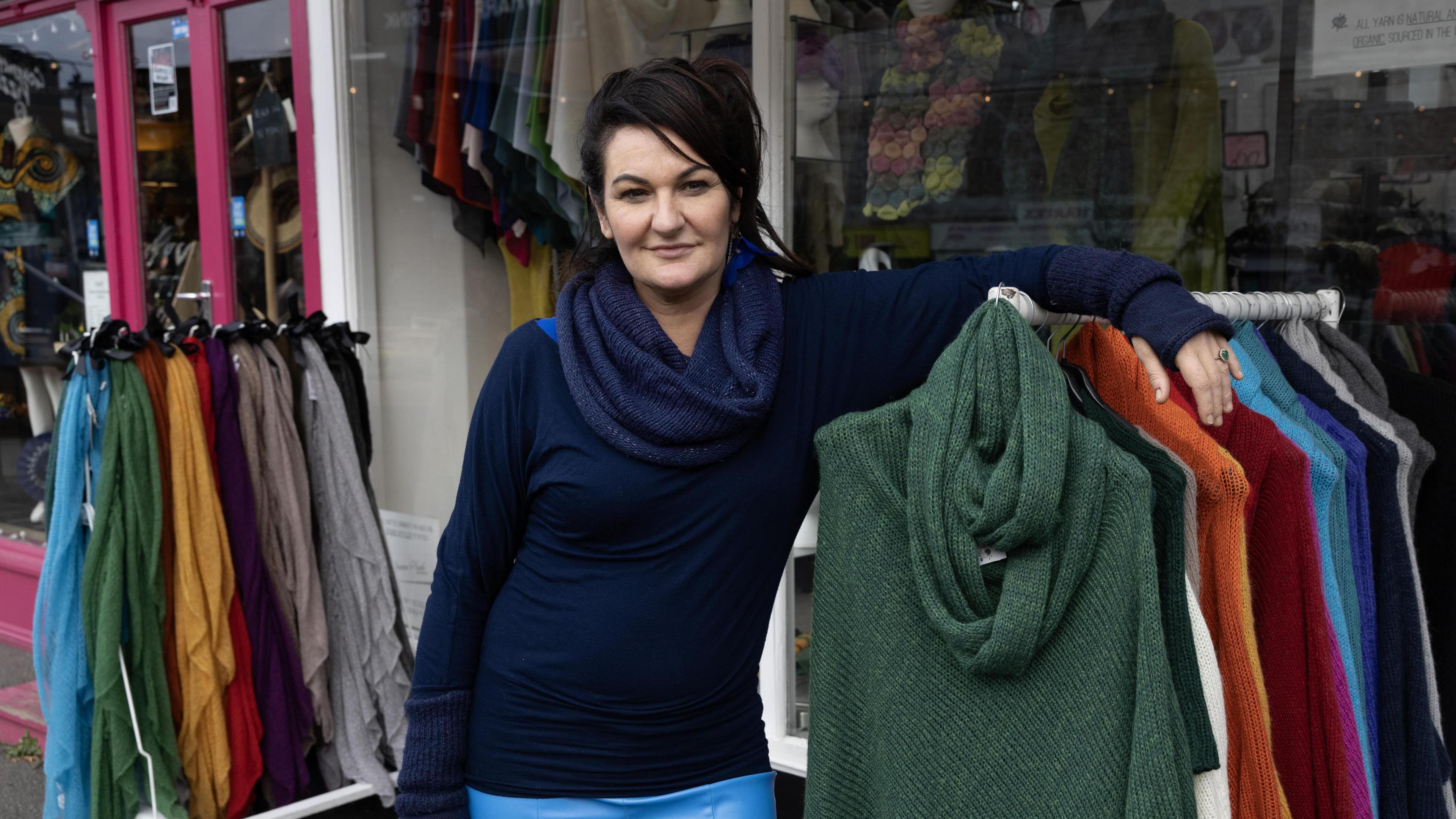 Joanne Plumb in a navy jumper leaning on a rail of knitwear outside her shop in Gabriel's Wharf.
