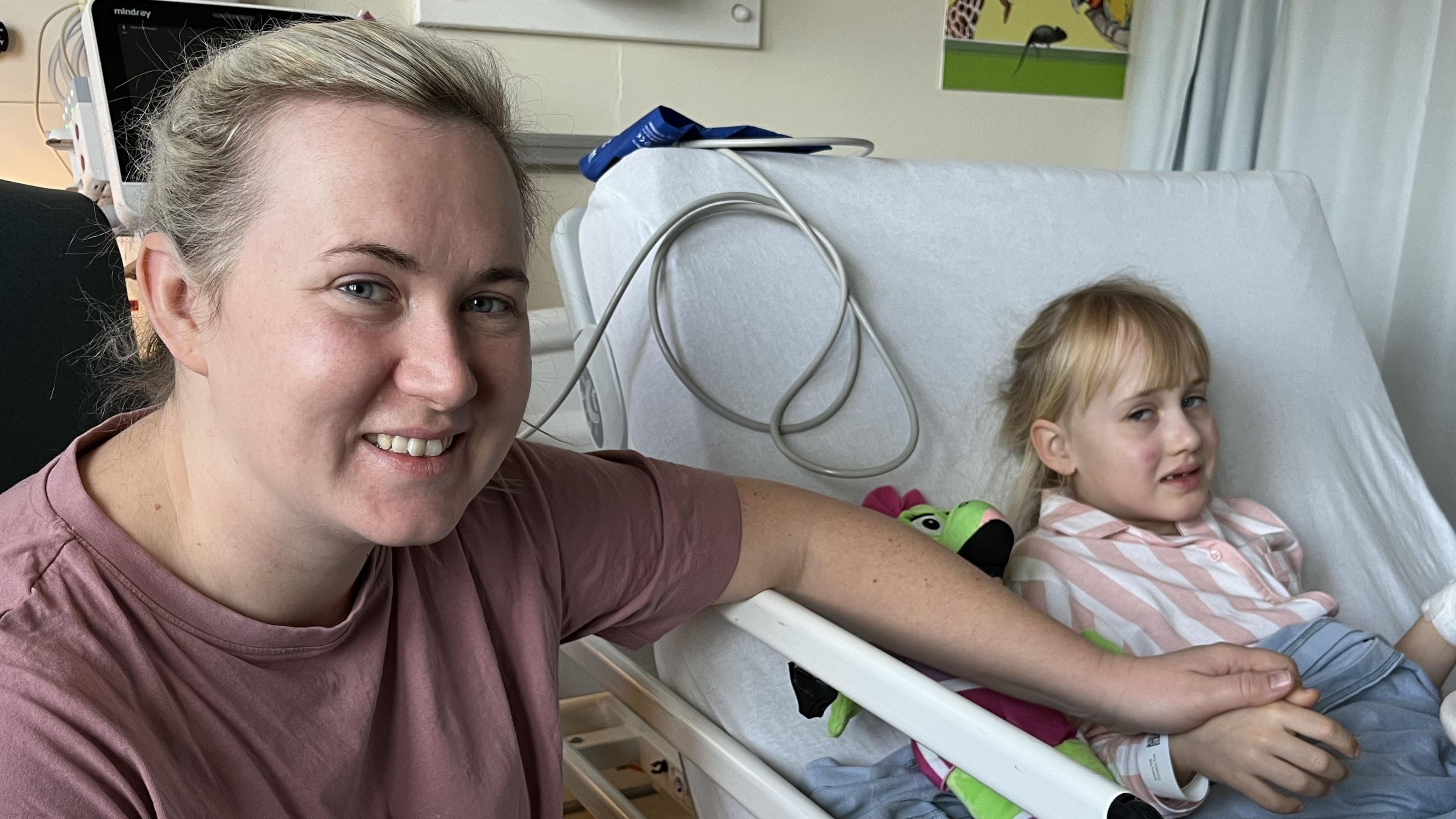 Mum, Charlotte, sat next to her daughter's hospital bed and holds her daughter's hand