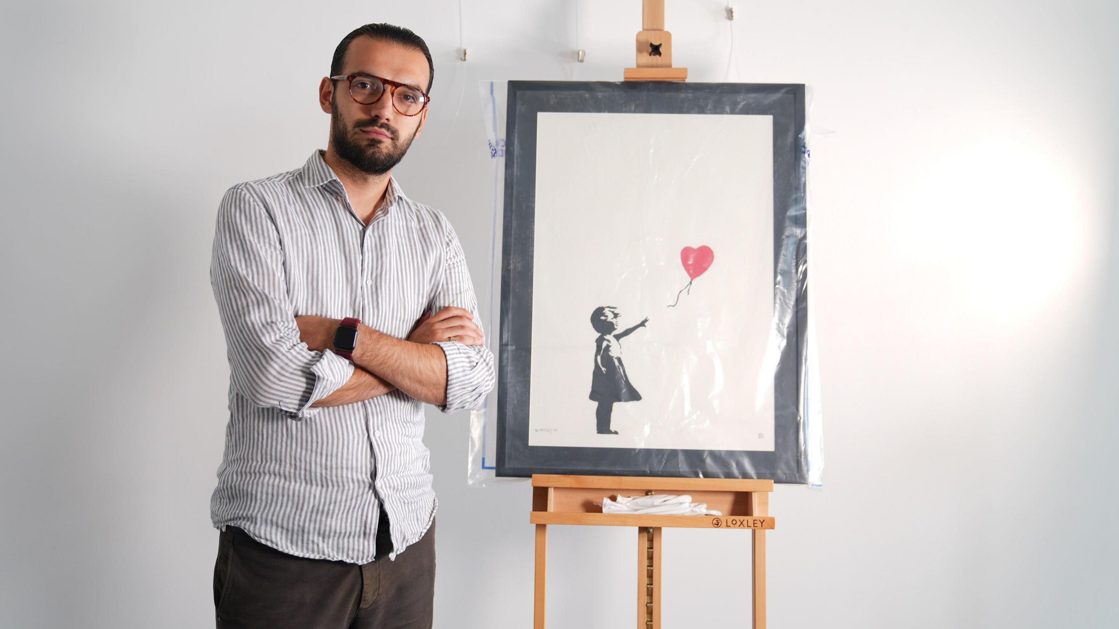 Gallery manager Lindor Mehmetaj stands with a Banksy painting, Girl With Balloon, at the Grove Gallery in London