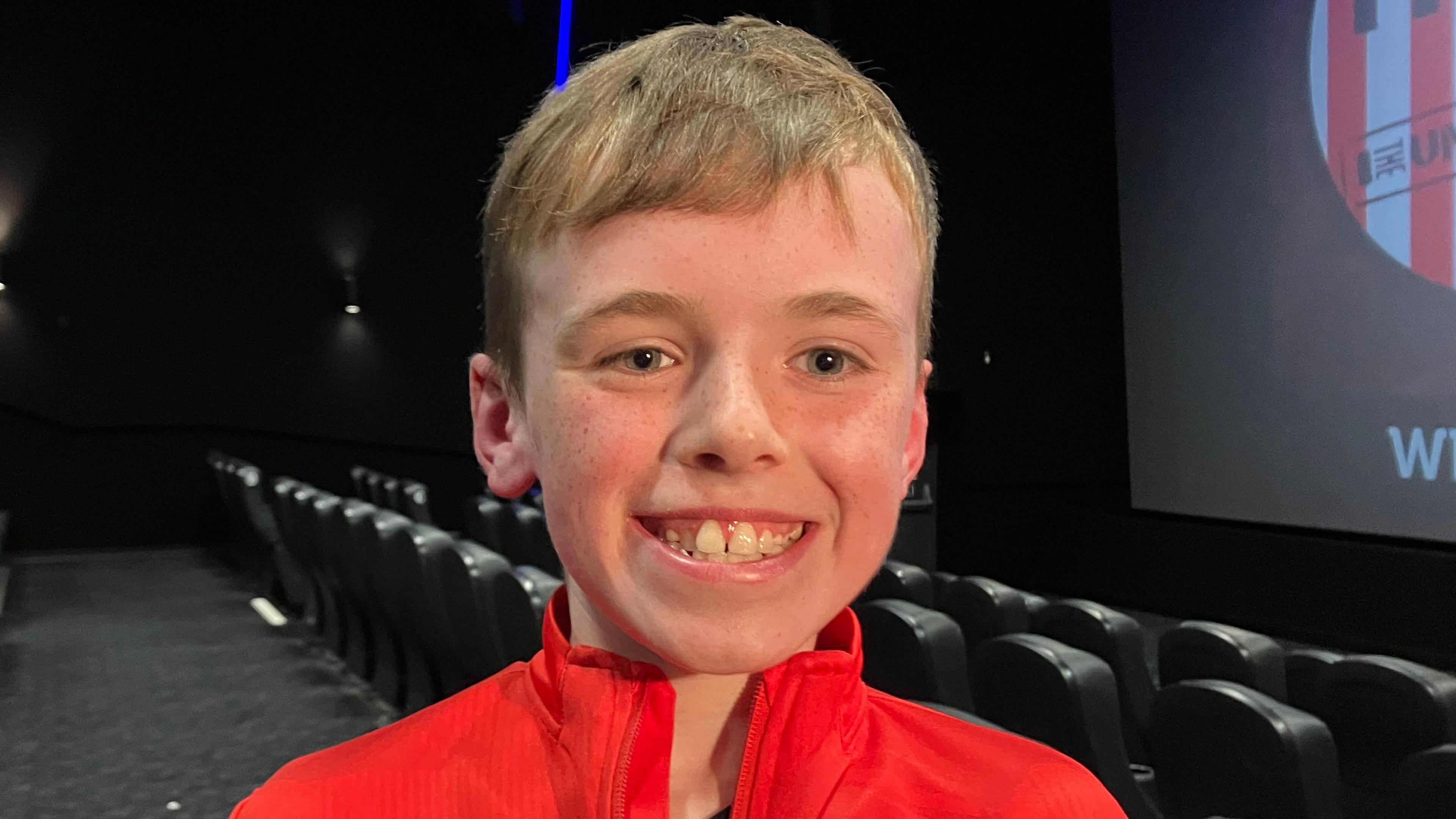 Logan is seen smiling from ear to ear inside a cinema.
He has short hair and is wearing a Derry City jacket.
A number of empty seats are seen behind him.