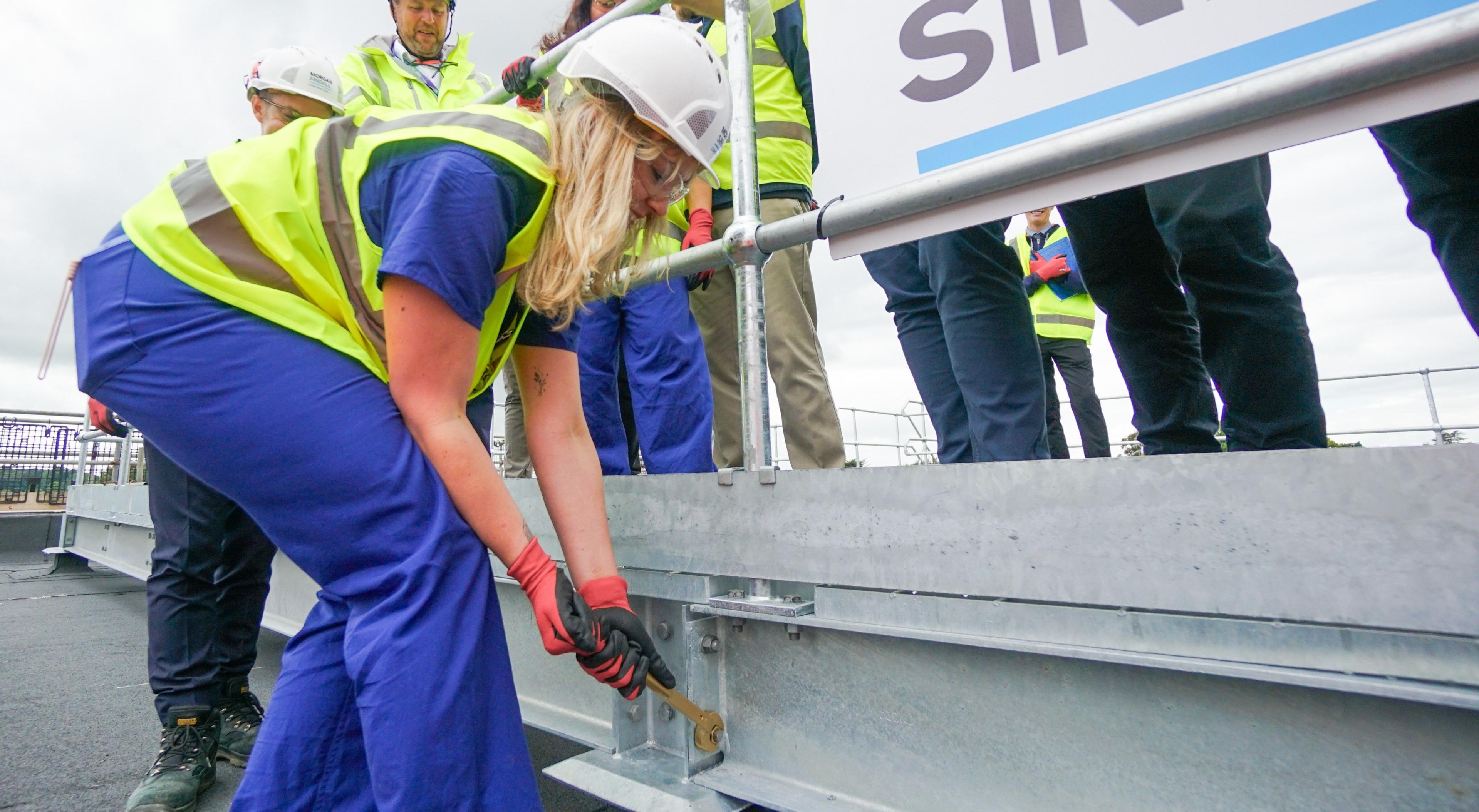 A woman wearing a hard hat and high vis tightening a bolt on a construction site