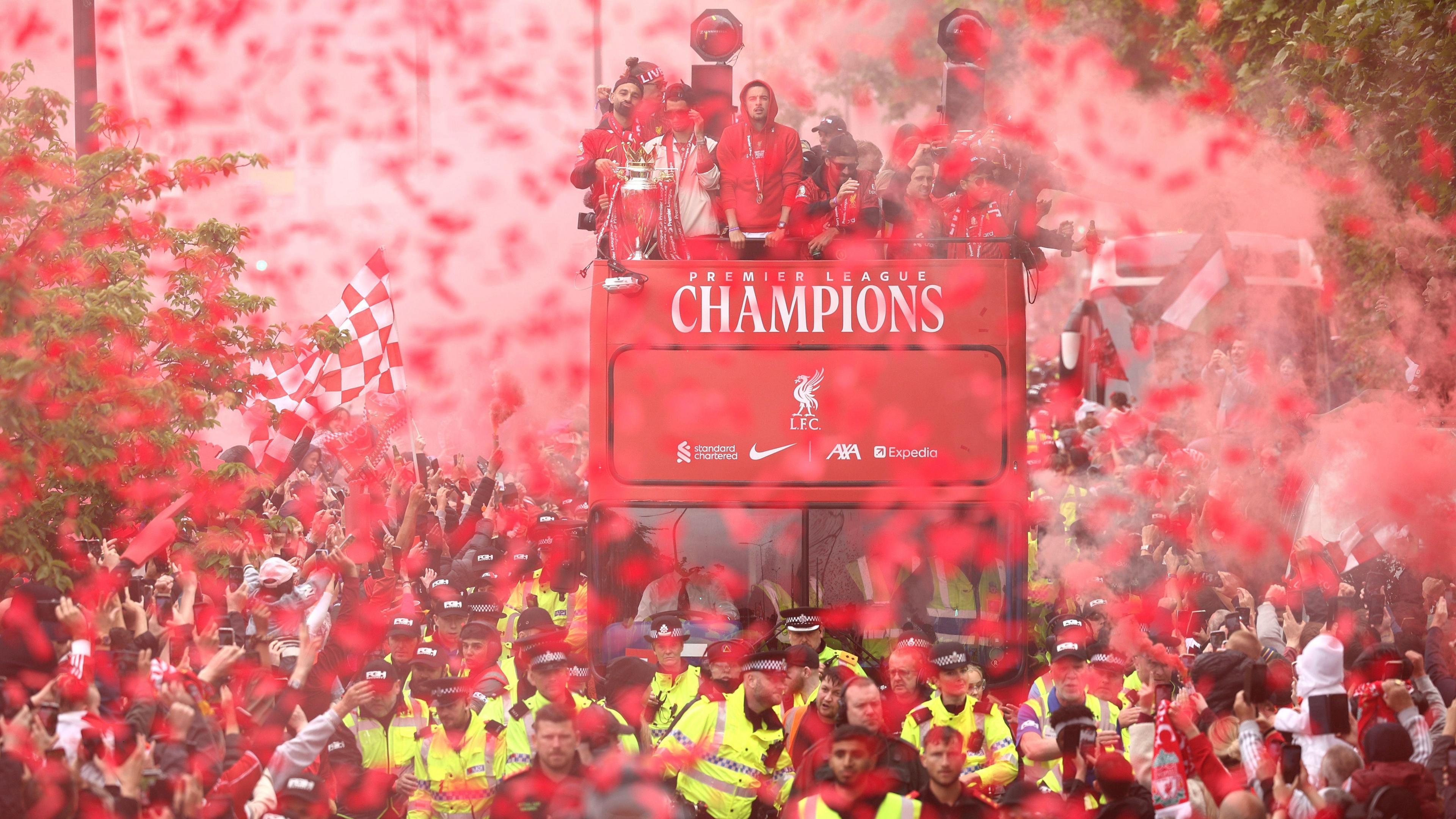 Liverpool players on their open top bus shrouded in red flare smoke with people packing the streets