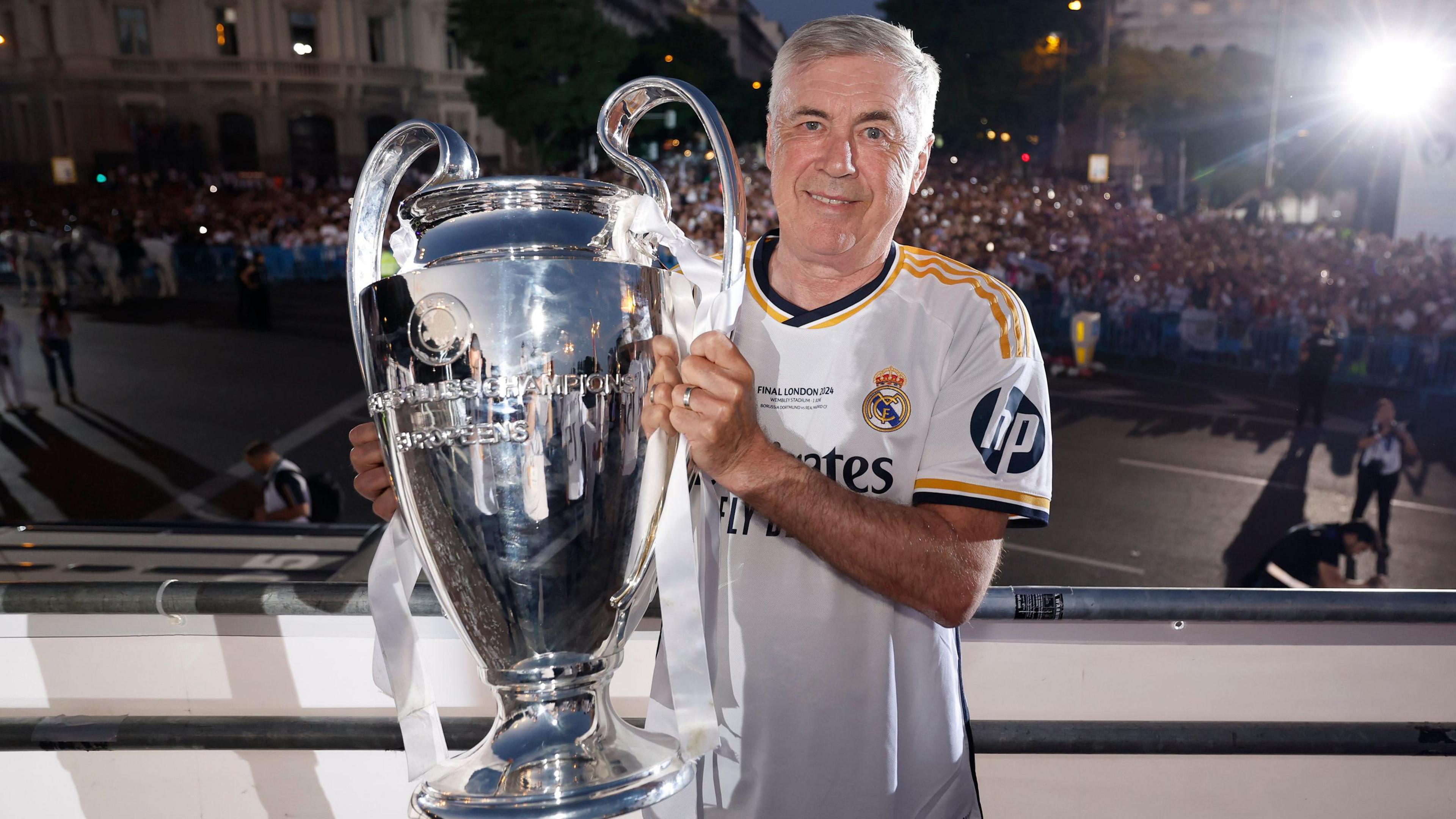 Carlo Ancelotti, in a Real Madrid shirt, holding the Champions League trophy