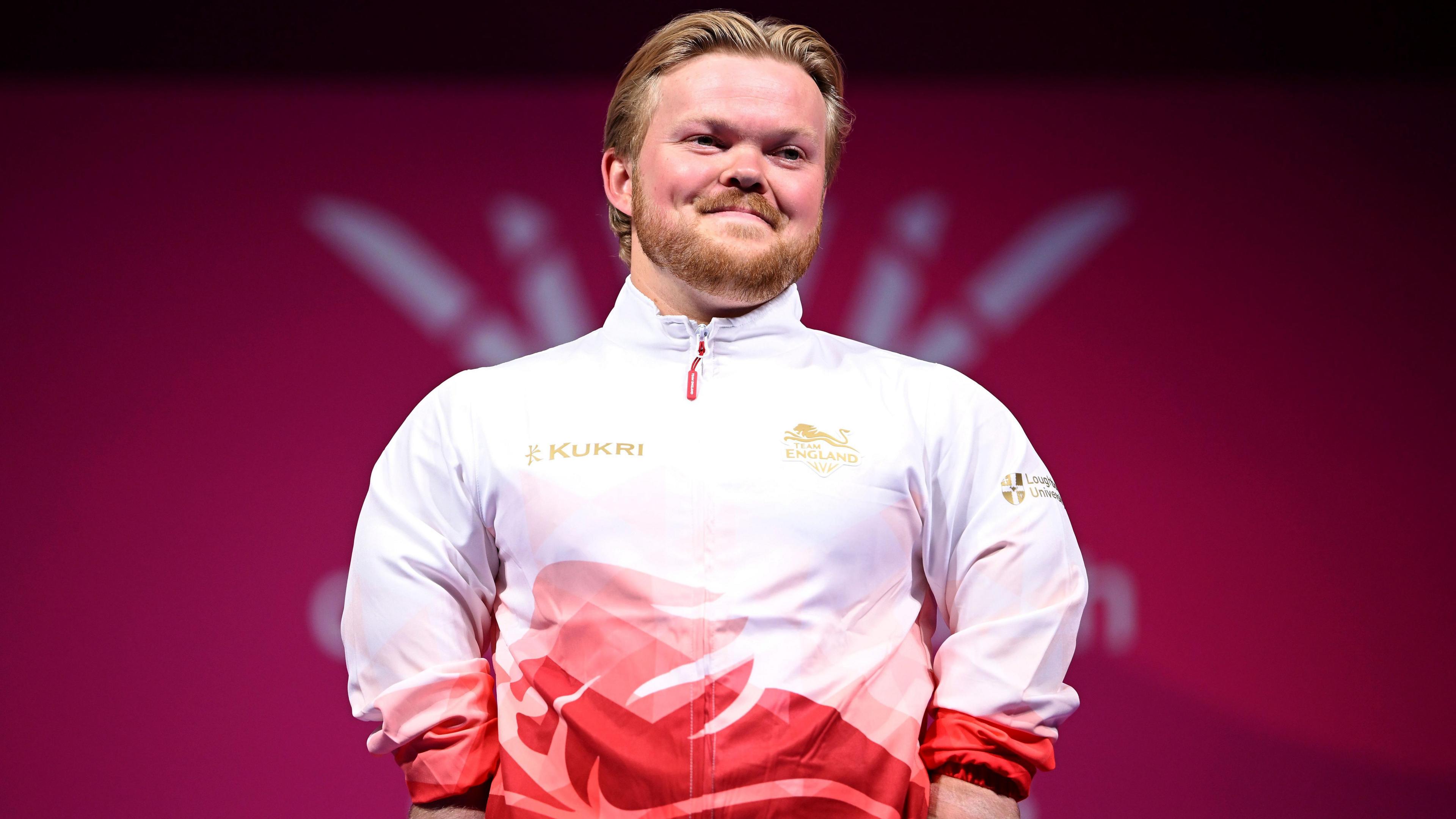 Mark Swan in red and white top standing on a podium, smiling.