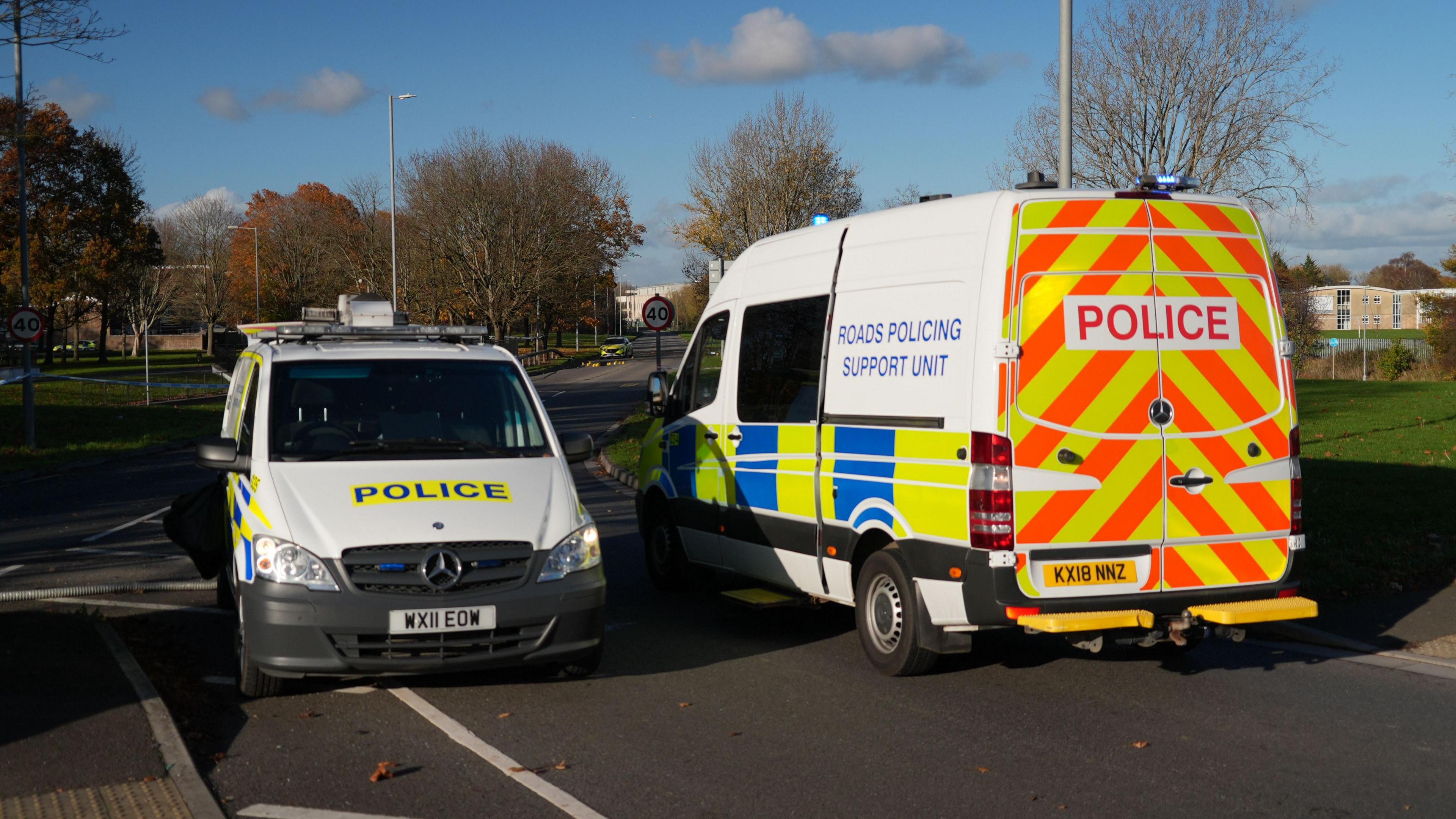 Two police vans parked up to block access to a road in Swindon following a suspected hit and run. The vans are facing opposite ways. They are both white with yellow, orange and blue stripes on them and the word "police" written in capital letters. 