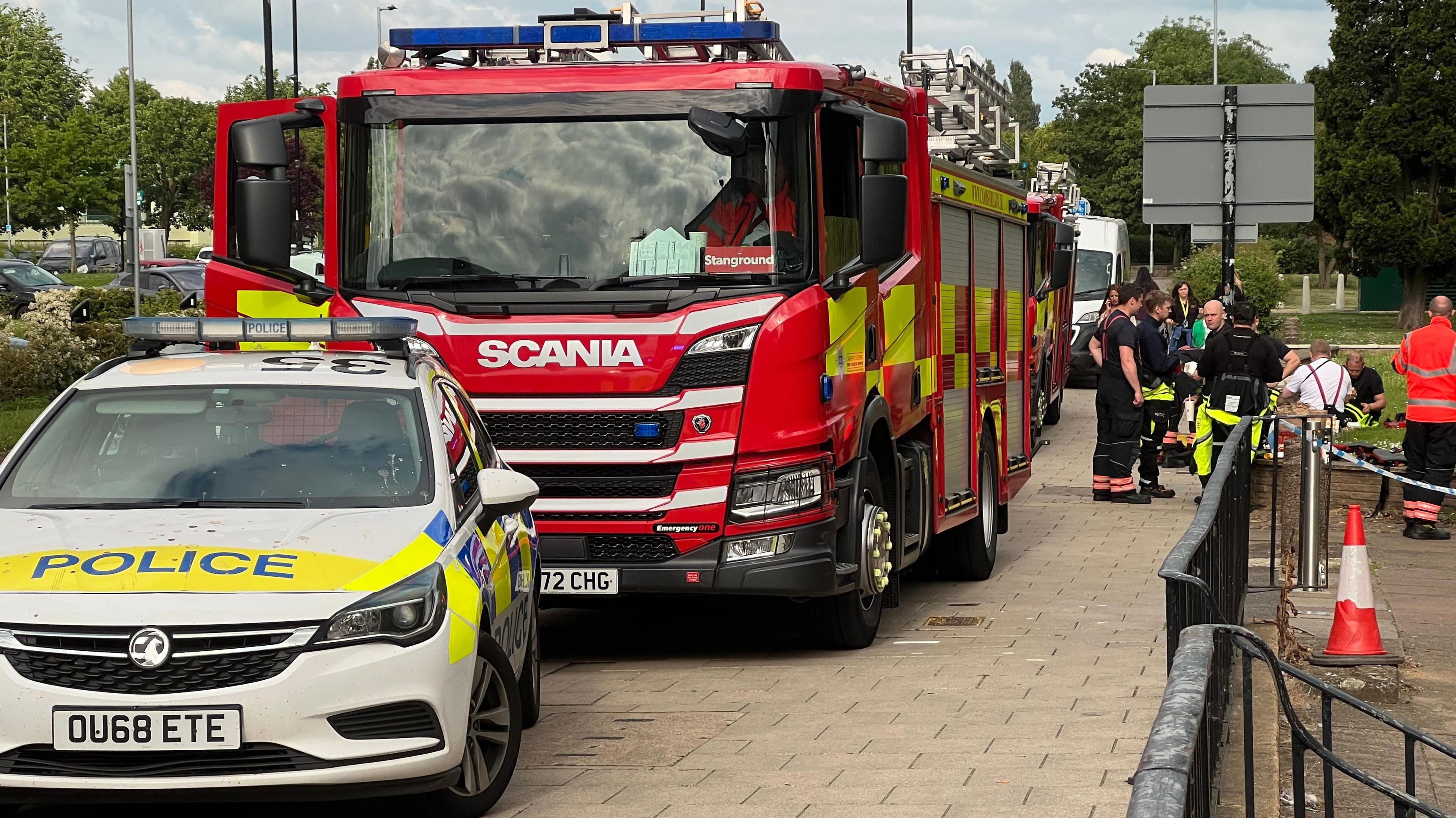 A marked police car, fire engine and a crowd of people