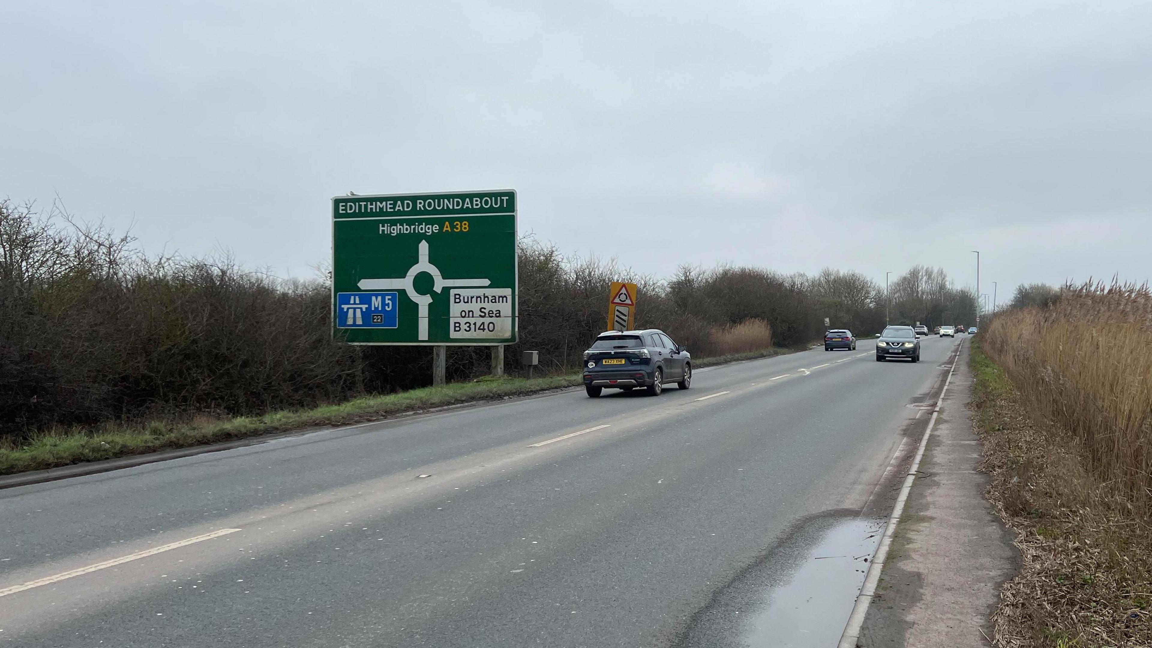 The A38, there are cars on both sides of the road and there is a sign signalling the approach of Edithmead roundabout.
