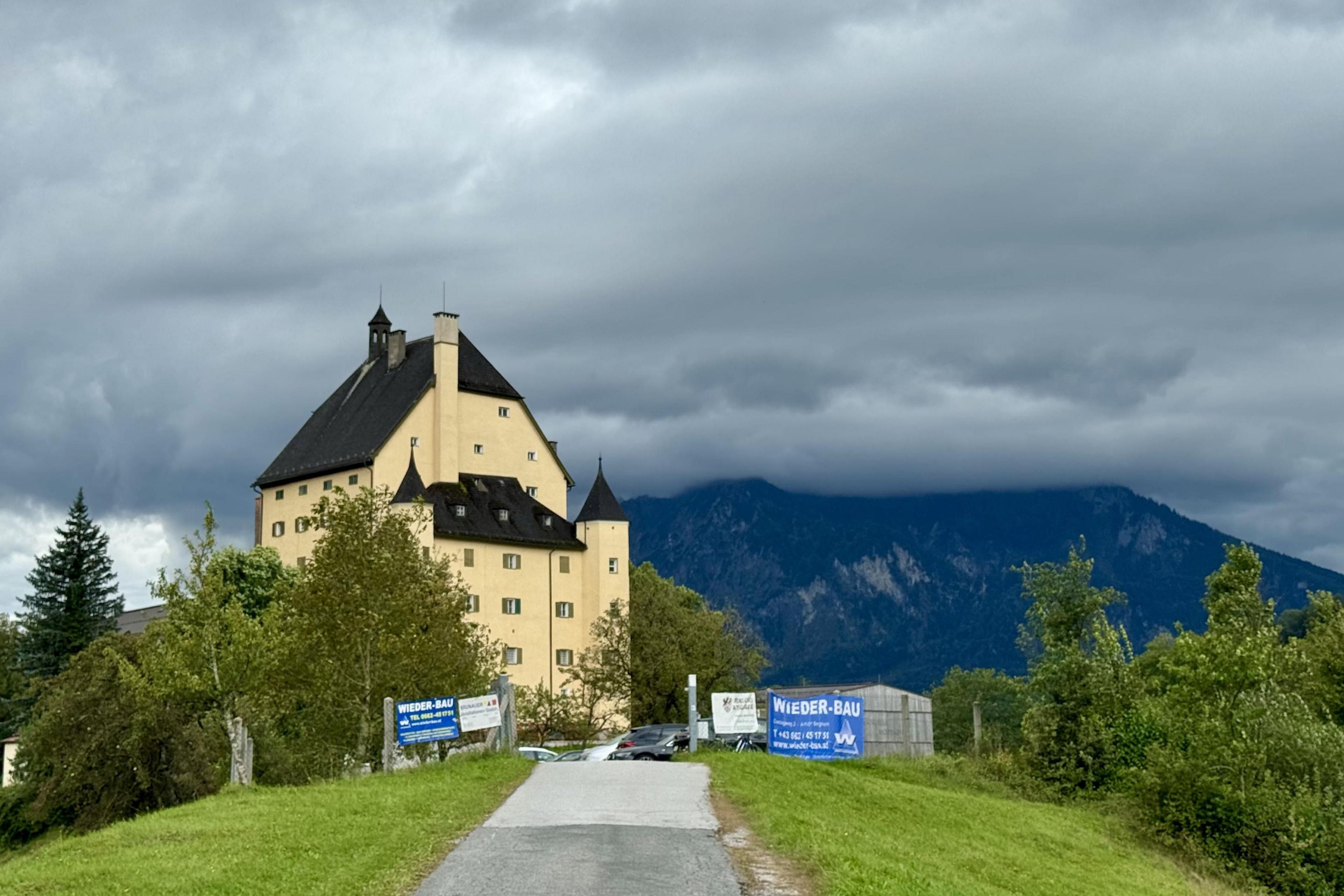 Schloss Goldenstein stands on a cloudy day overlooked by the Austrian Alps