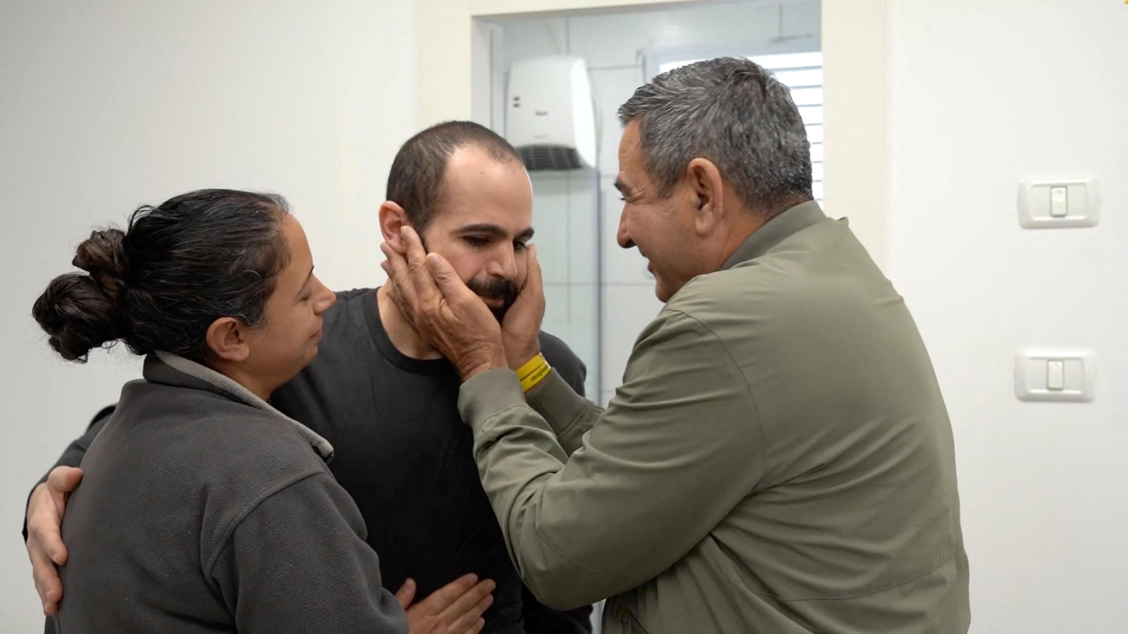 A man in a khaki jacket holds Yarden Bibas's face as he embraces a relative after being released from Hamas's captivity. 