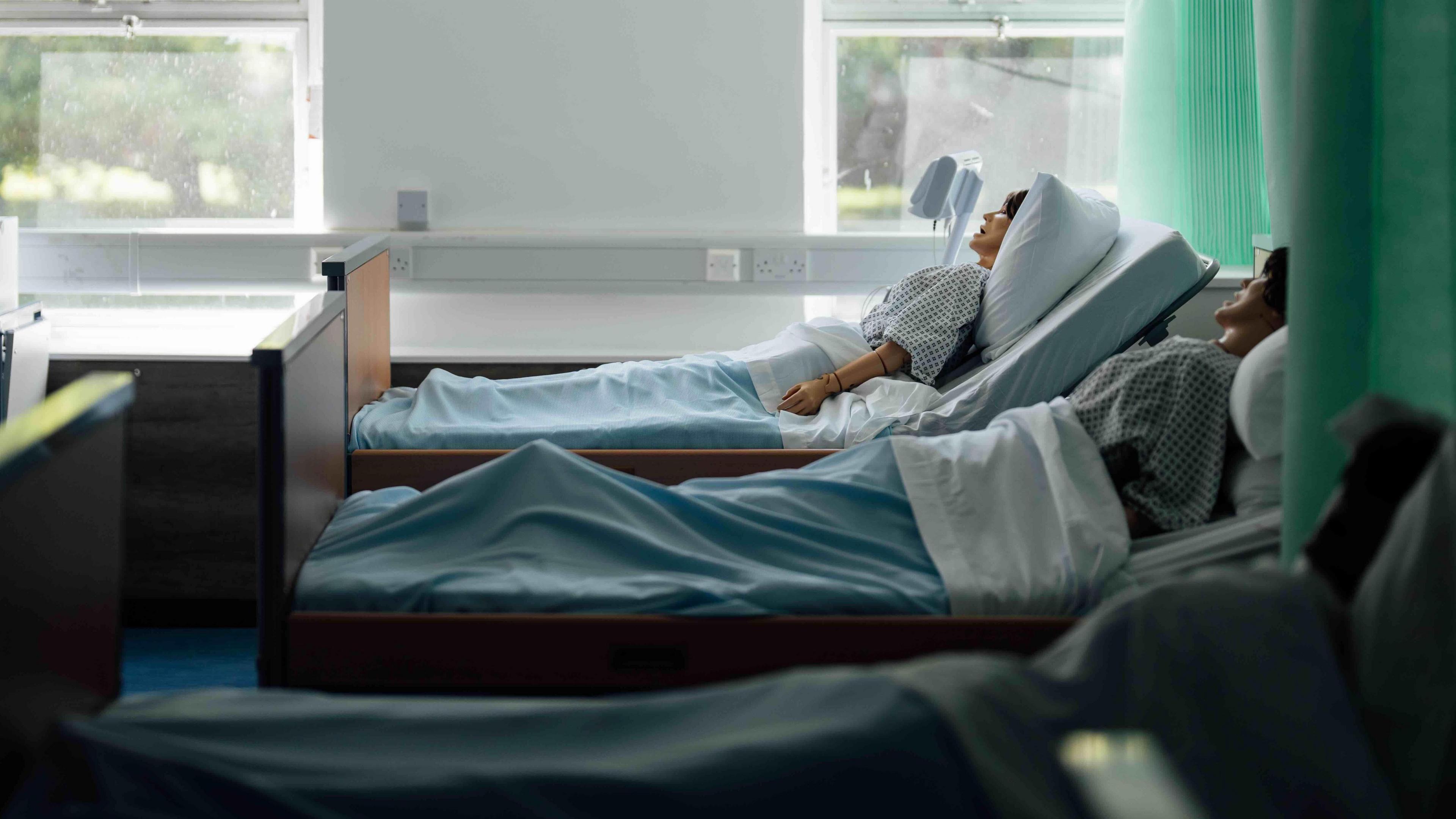 A row of three dummies are laying in hospital beds in a health clinic.