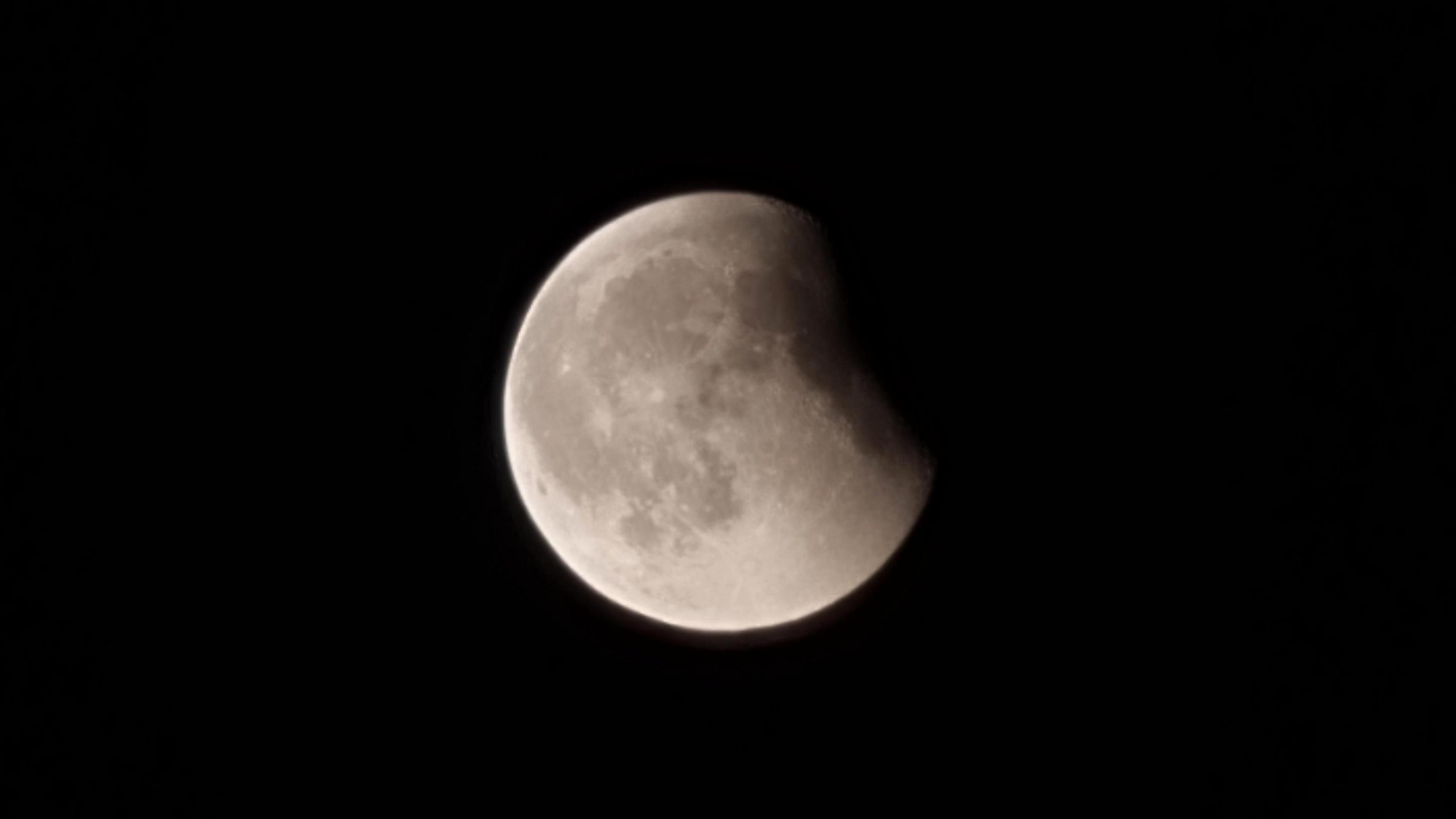 A white moon against a black sky. The moon is partially eclipsed.
