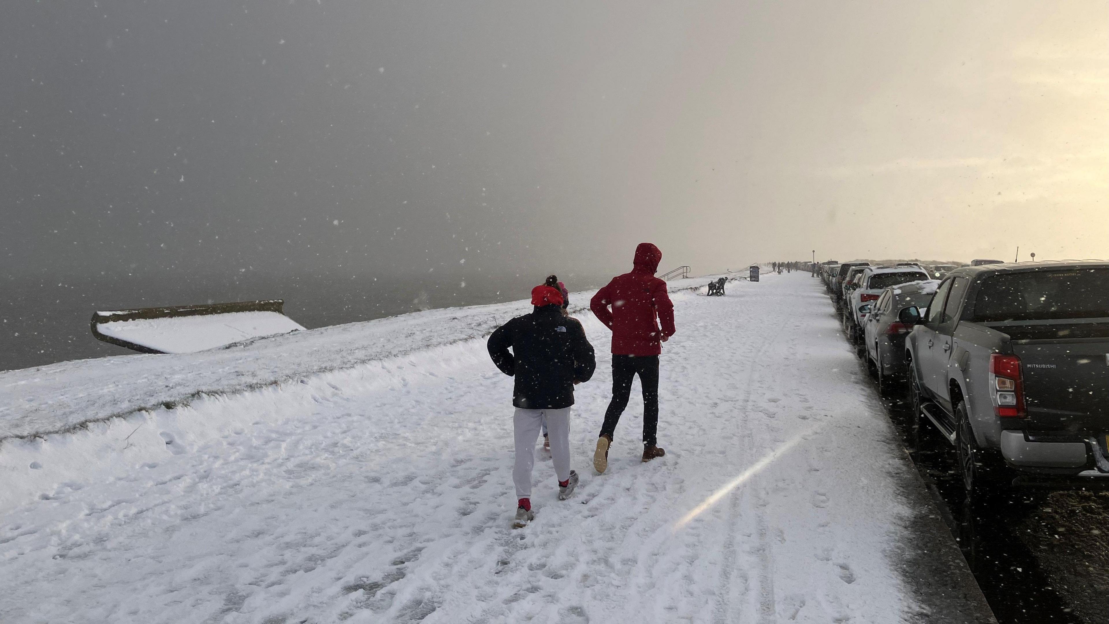 Snow falling and people walking along Aberdeen's beach boulevard. There are two people in winter clothing walking along.