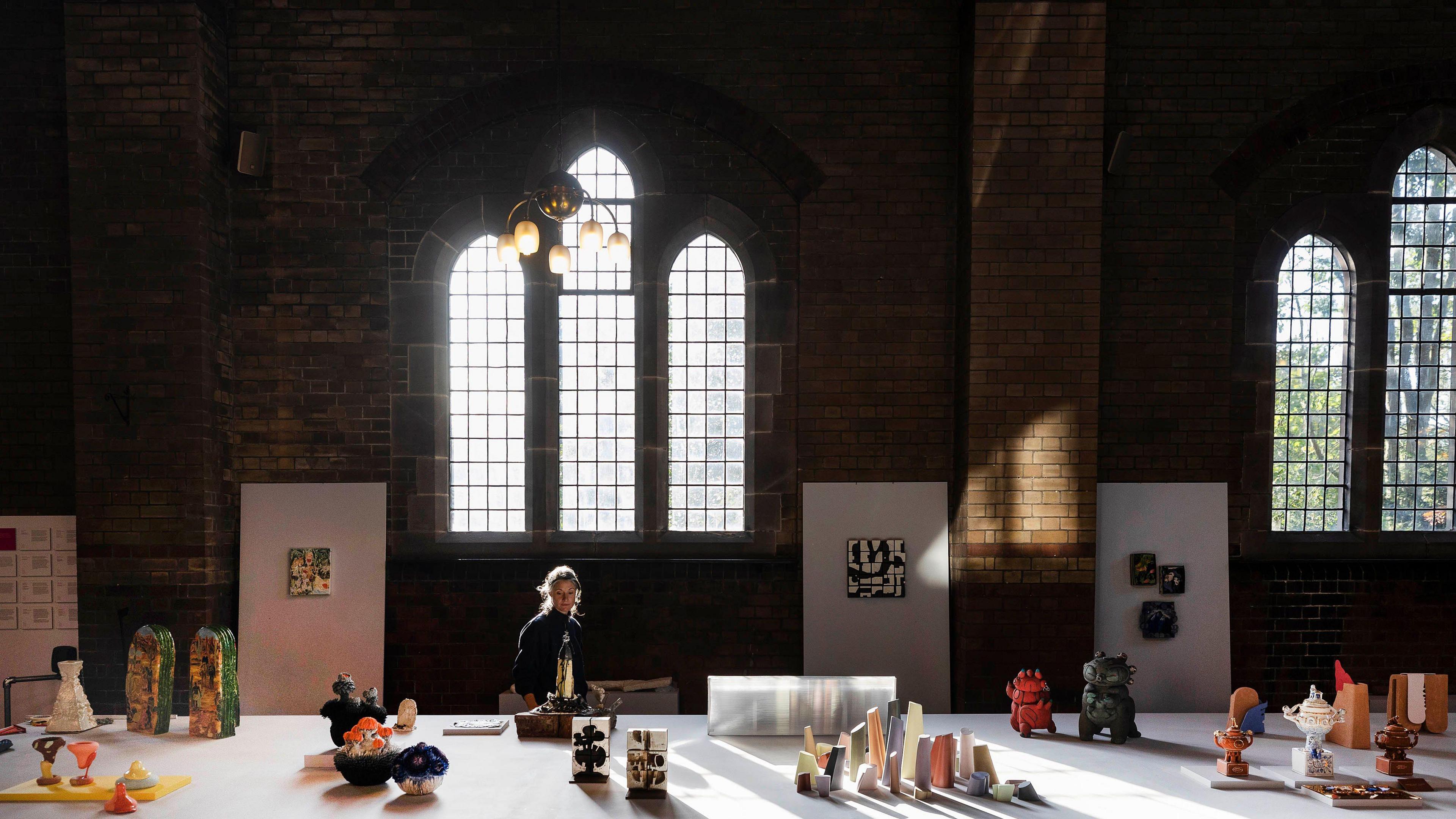 A large hall inside a church building with various ceramic models displayed on a big white table. A woman can be seen looking at the display.