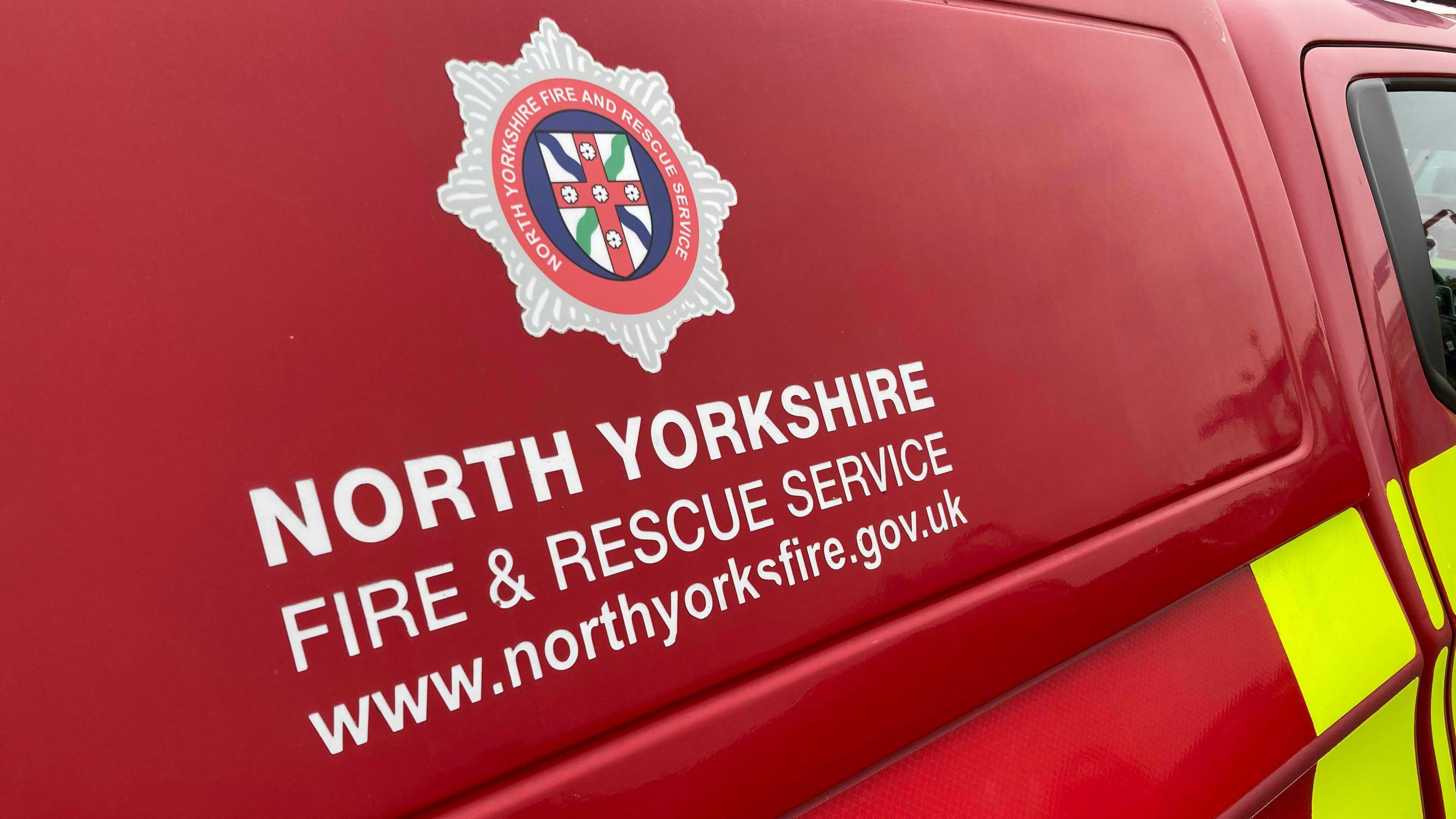 A red fire service vehicle with the crest of North Yorkshire Fire and Rescue Service and the service's name written on the van in white.