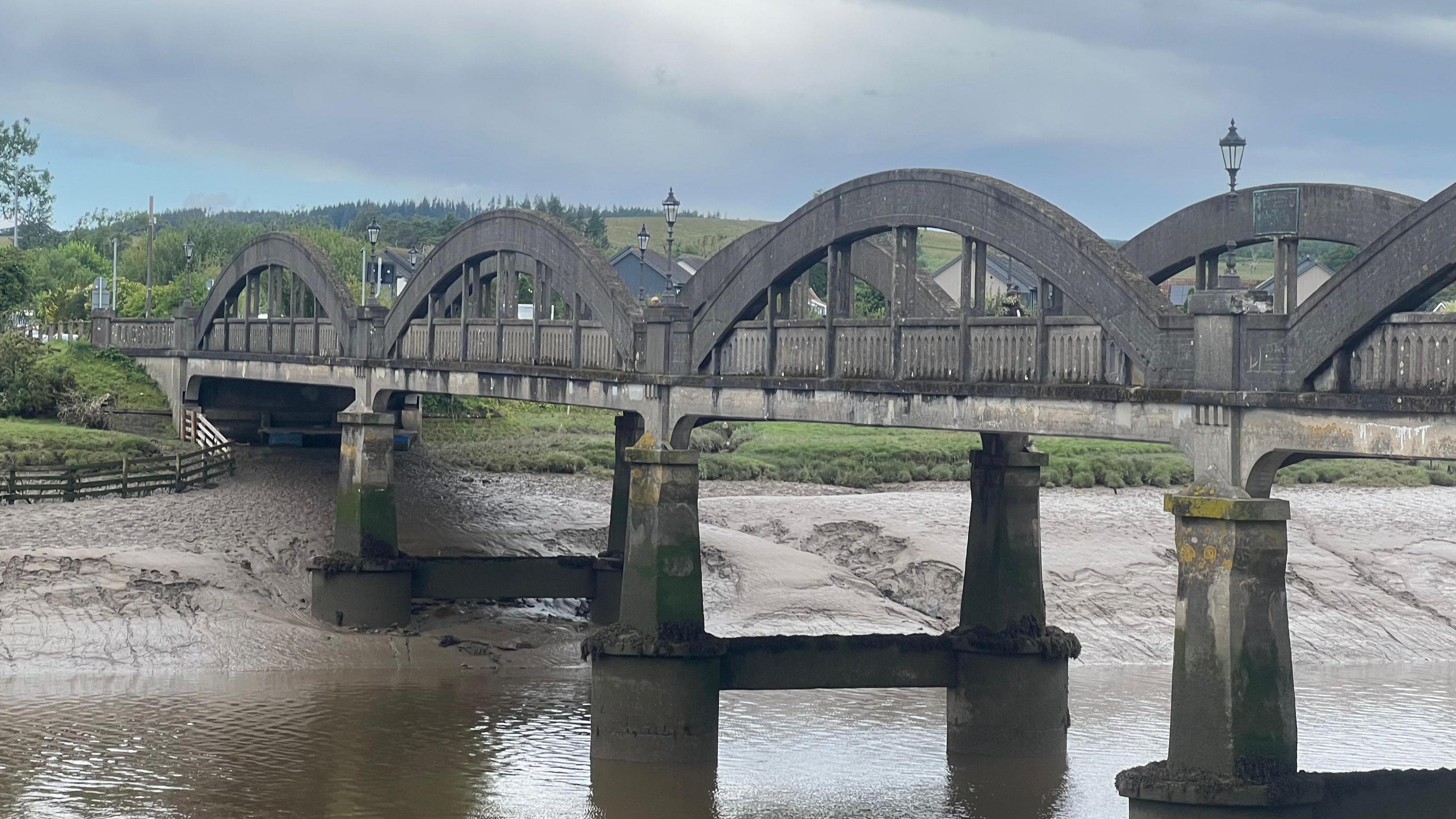A greying stone bridge crossing the river with a reflection