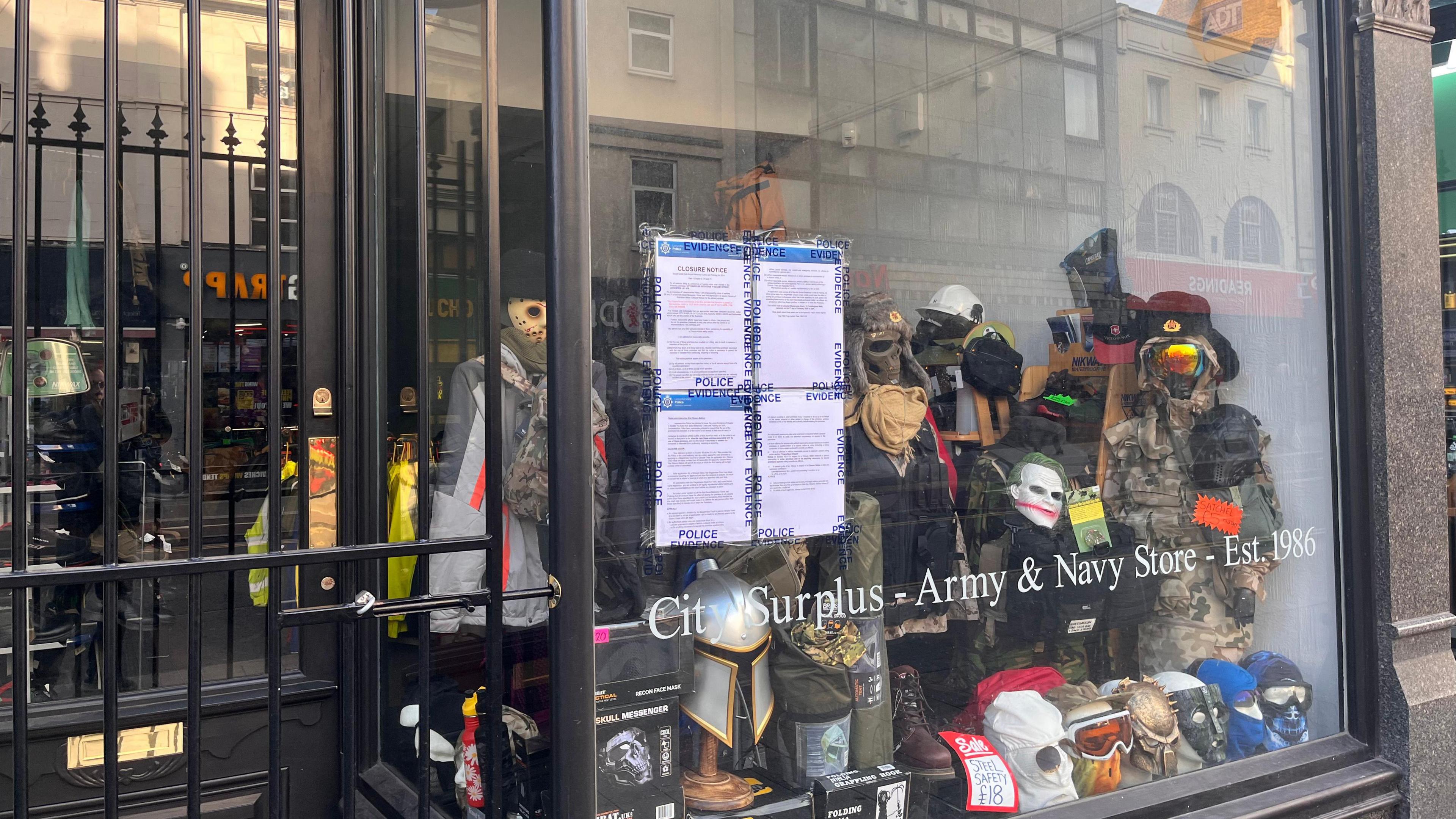 A shop window with four police noticed placed in it.  In the shop are masks and military headwear