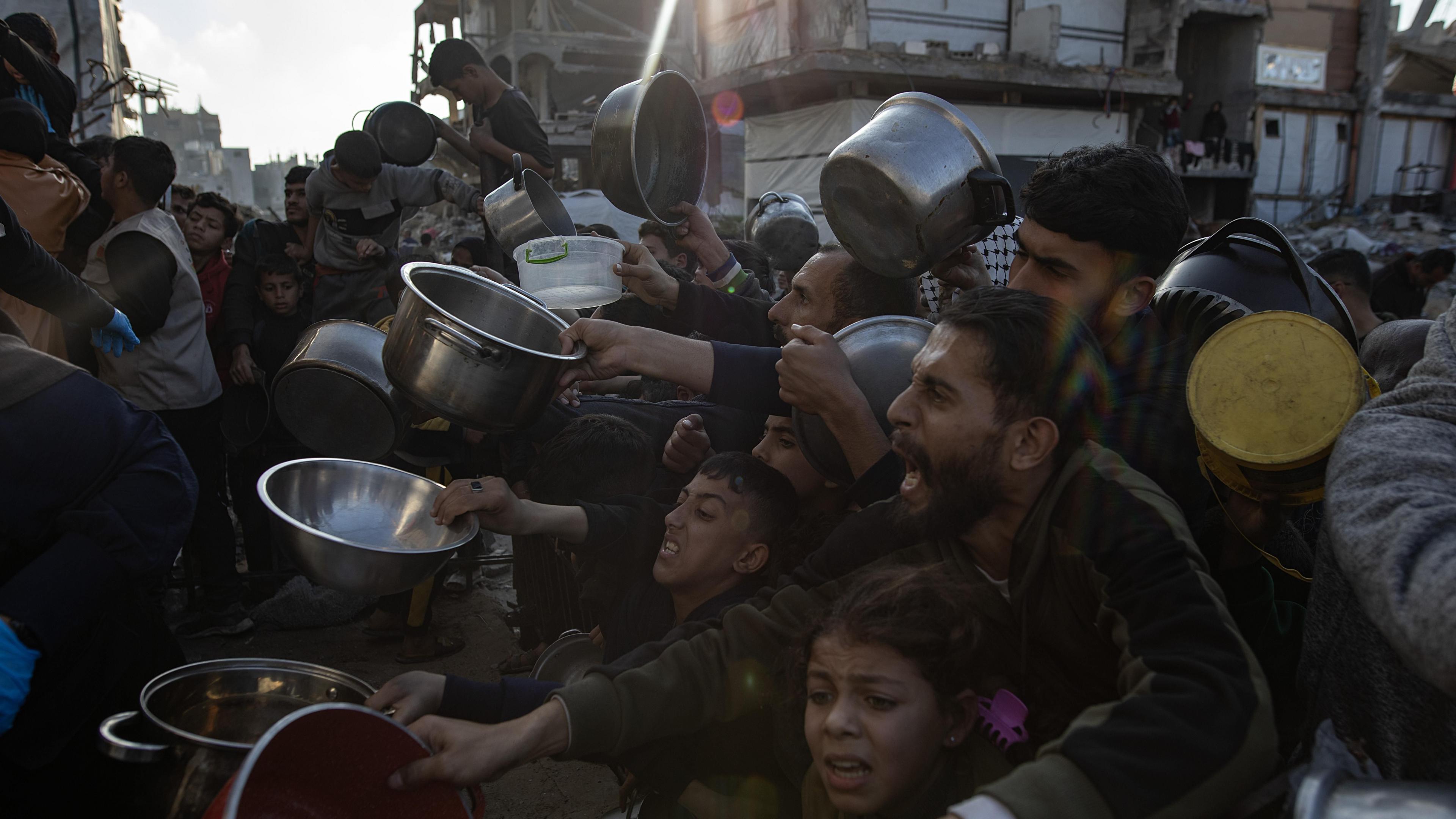 Internally displaced Palestinians hold out bowls to receive Ramadan meals from a charity kitchen in Beit Lahia in the northern Gaza strip