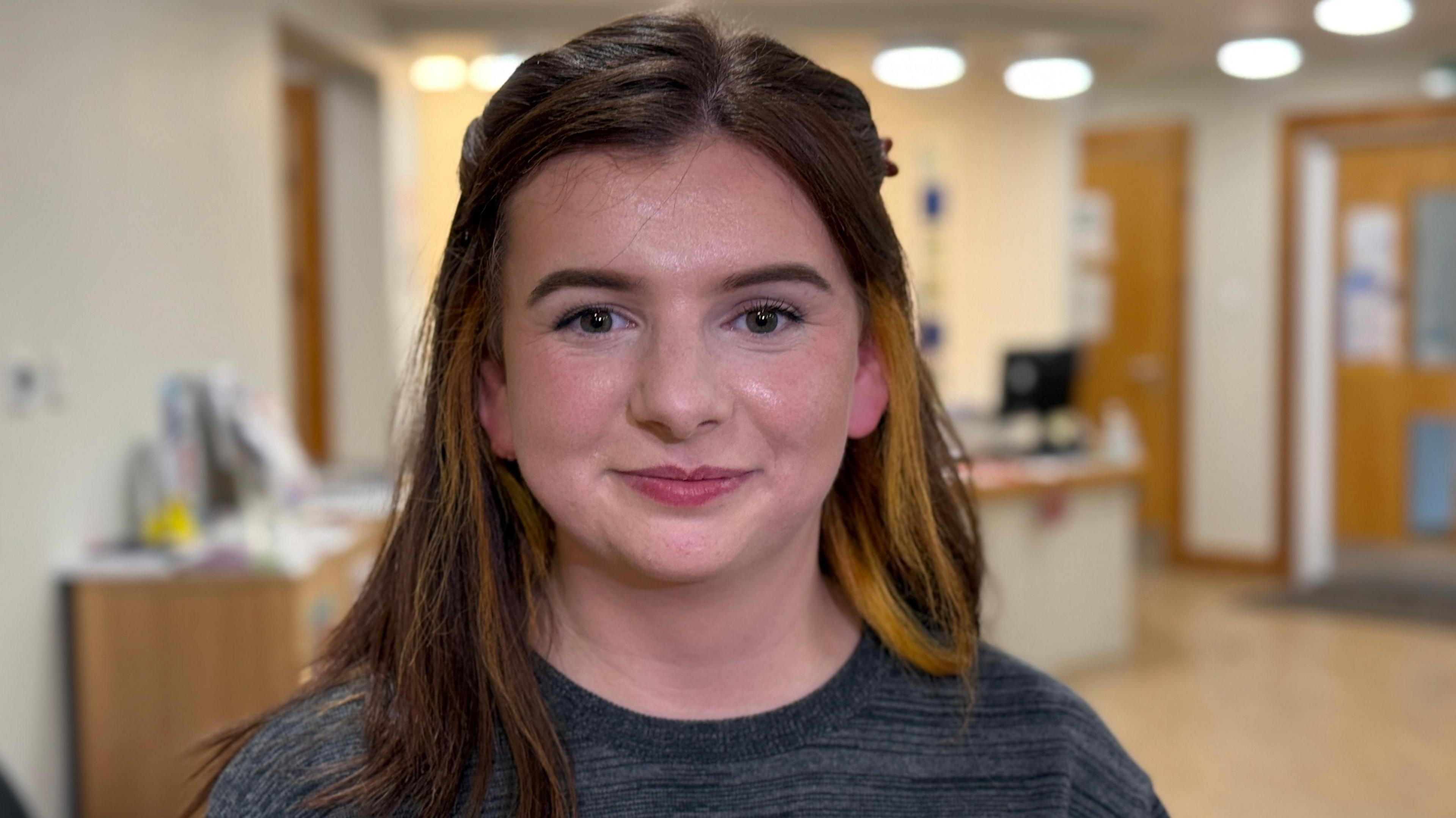 Hannah with medium length dark brown hair. She is wearing a grey Christmas jumper and looking directly at the camera.