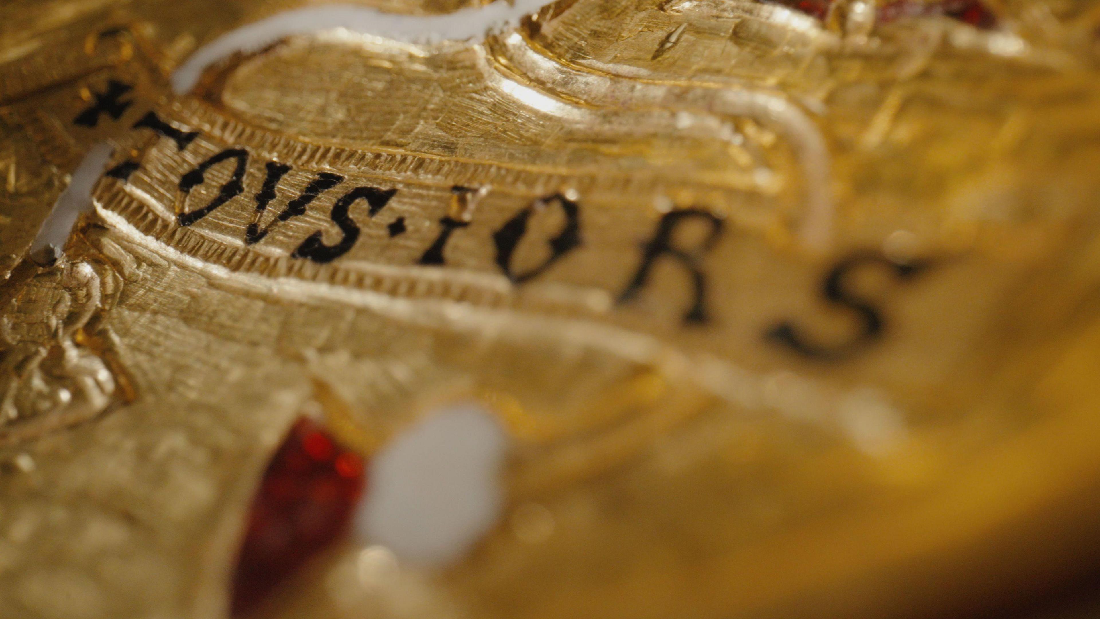 A close up of a gold pendant that reads "tousiors"