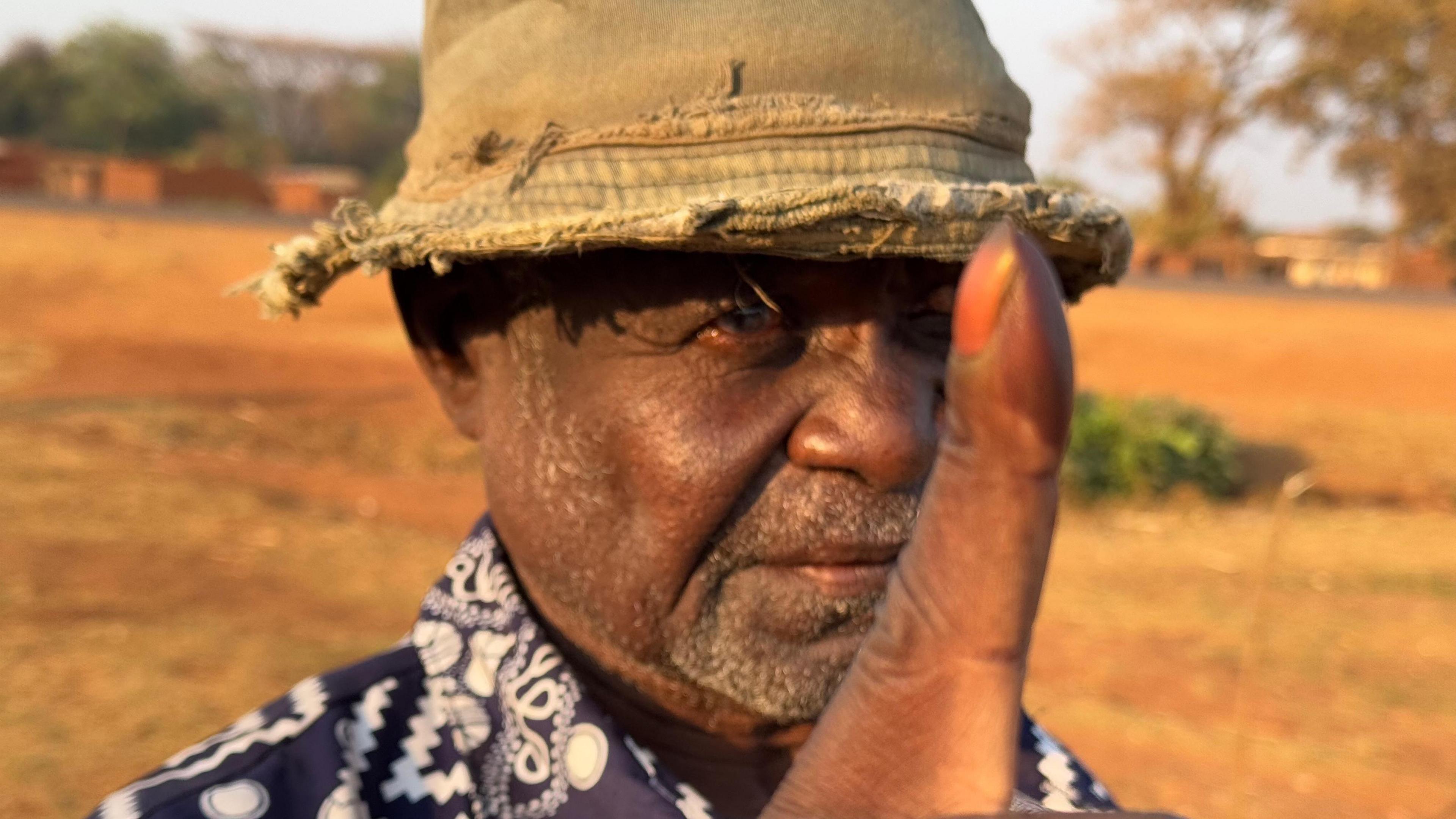 A head shot of a man, wearing a battered, khaki, cloth hat