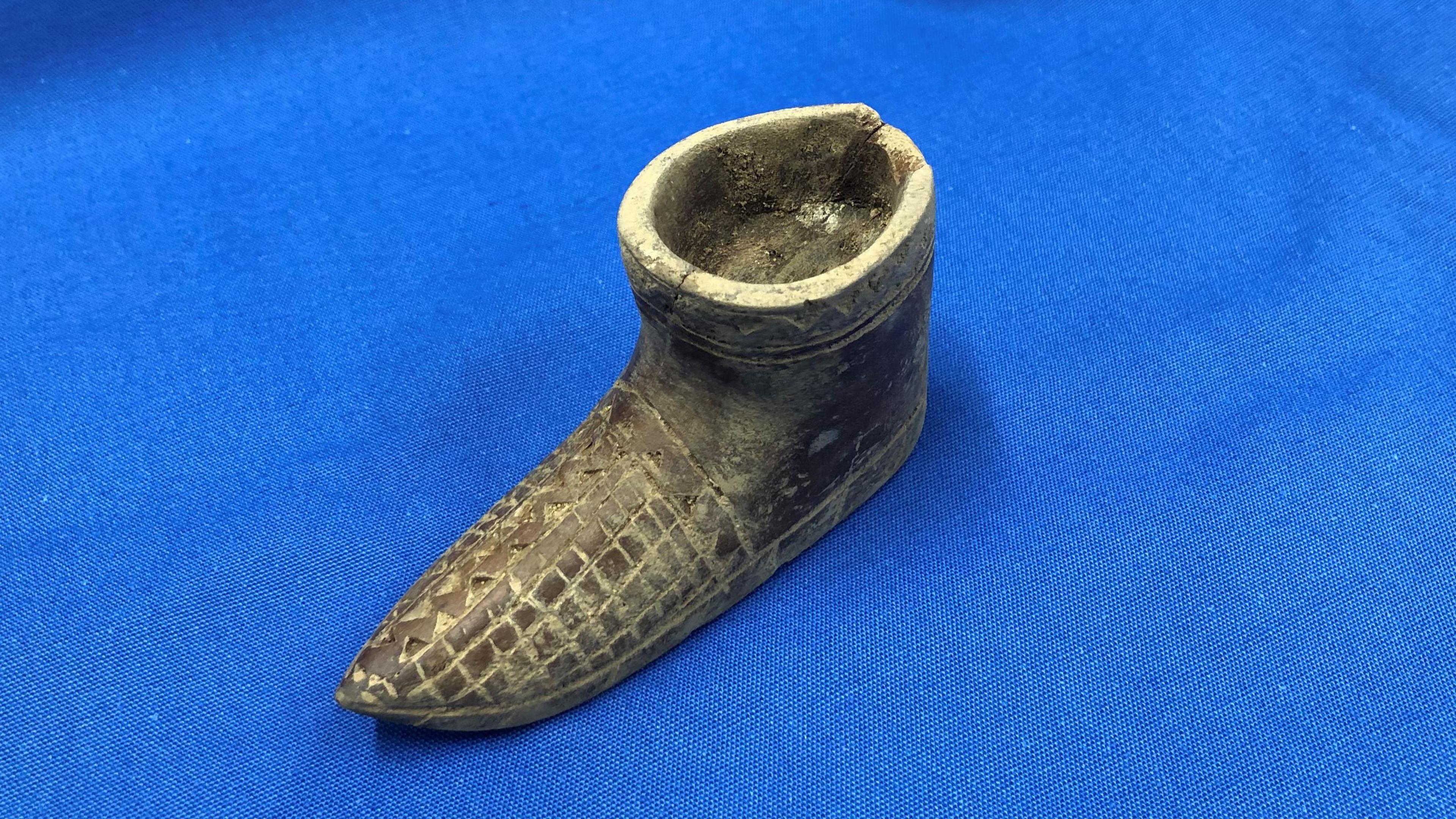 A tiny wooden shoe with an engraved pattern on the toes. The shoe is not hollow