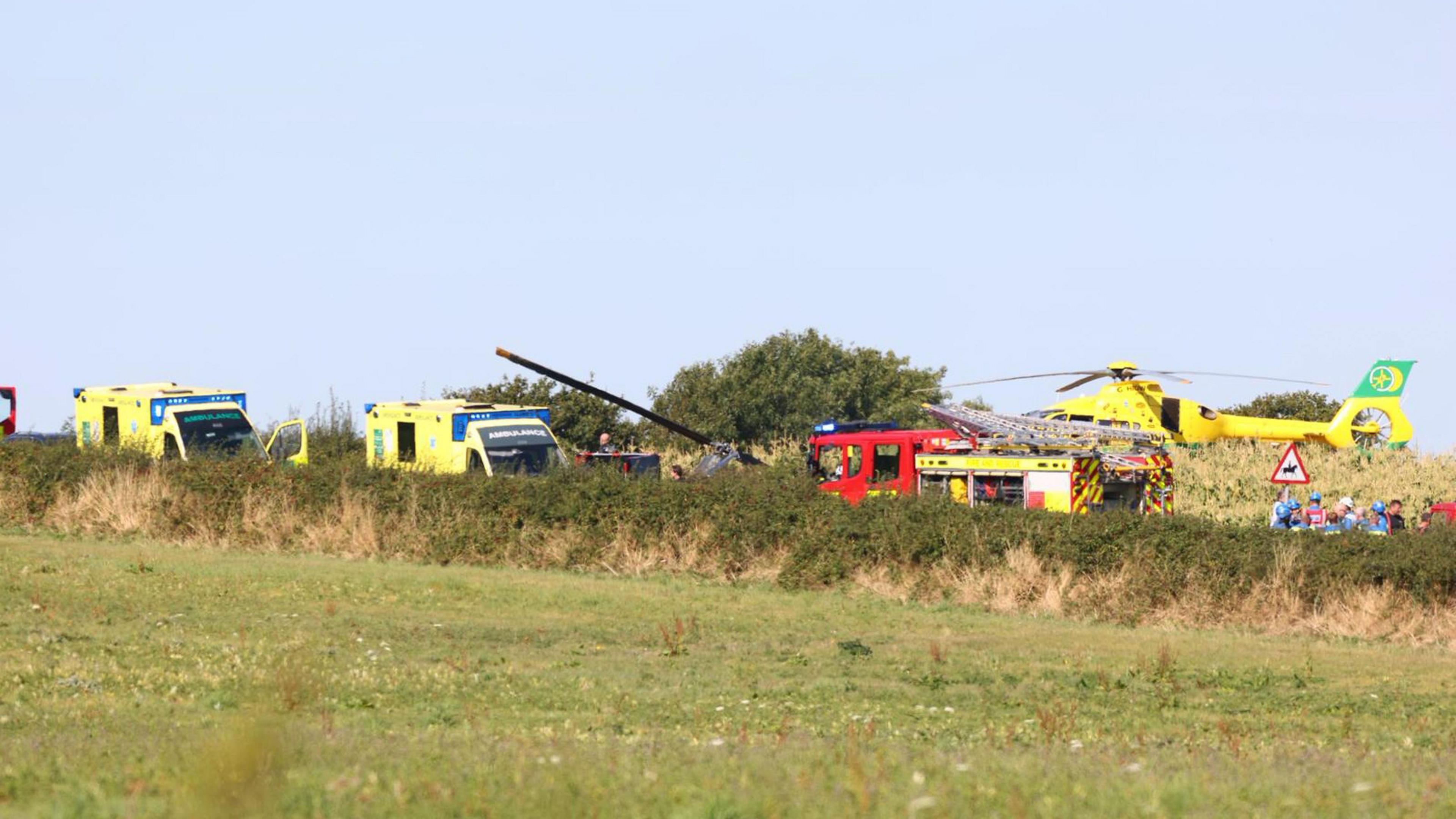 Emergency service vehicles can be seen on the road near a green field