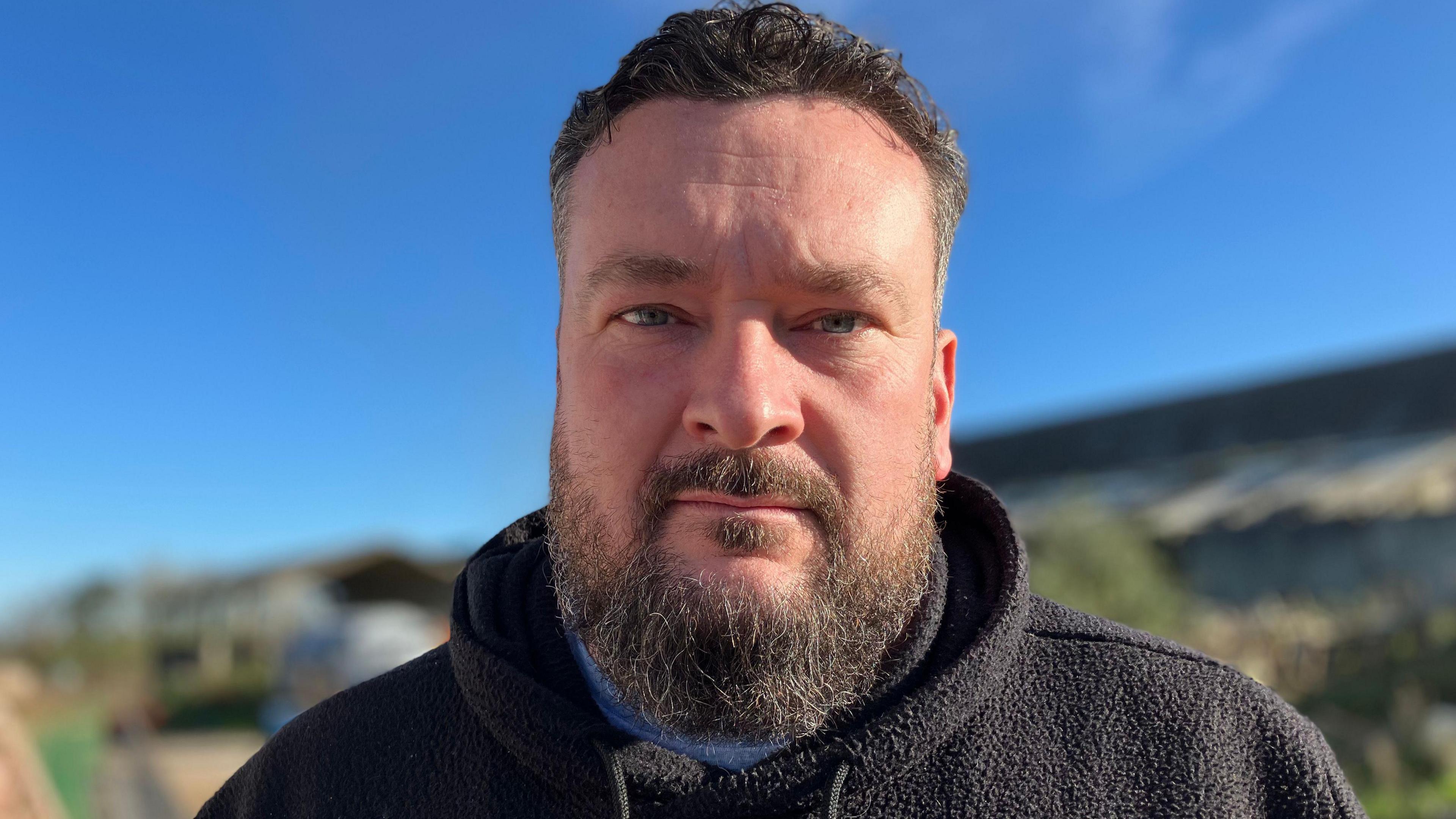 A bearded man looking at the camera with a neutral expression.