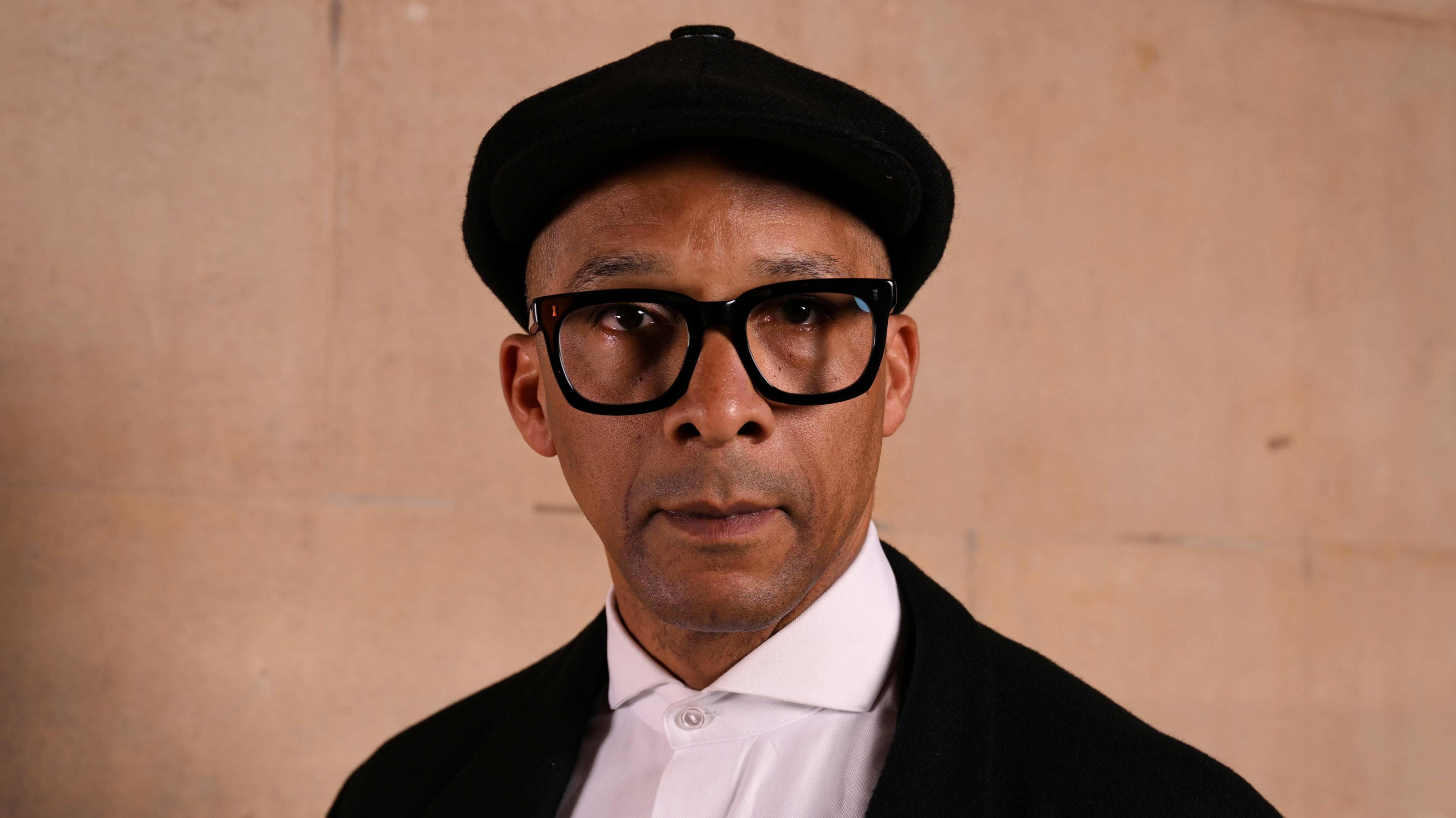 Jay Blades wearing a black cap, black jacket and white shirt