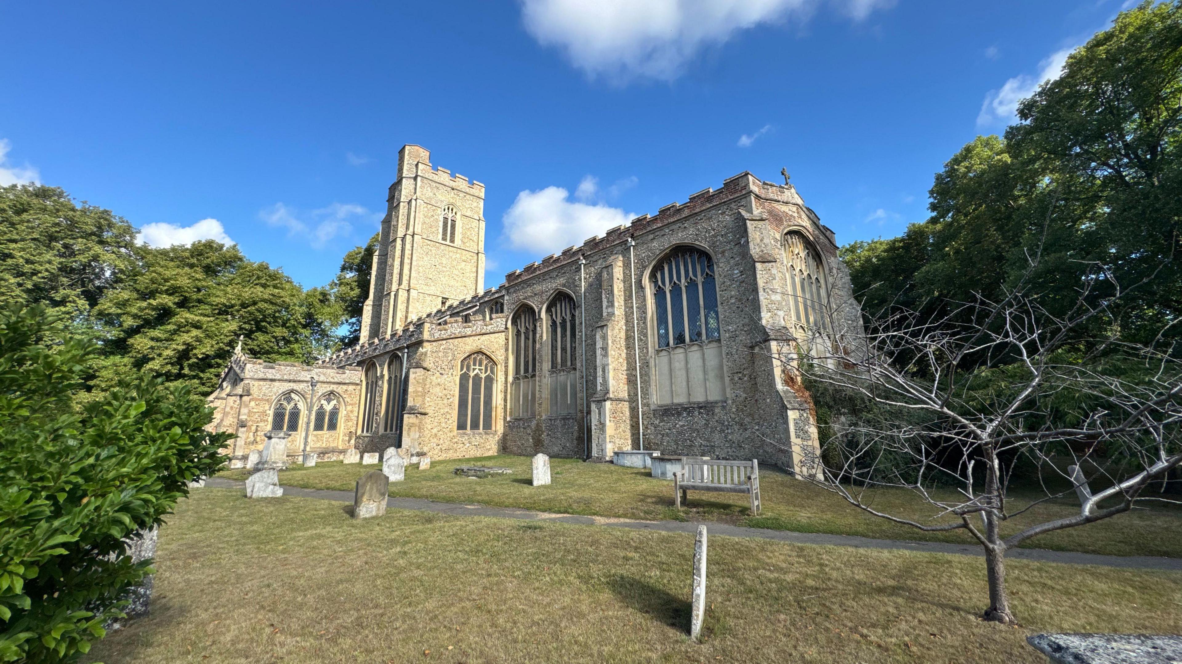 A wide-angle shop of St Gregory's church in Sudbury. It is surrounded by gravestones and trees. 