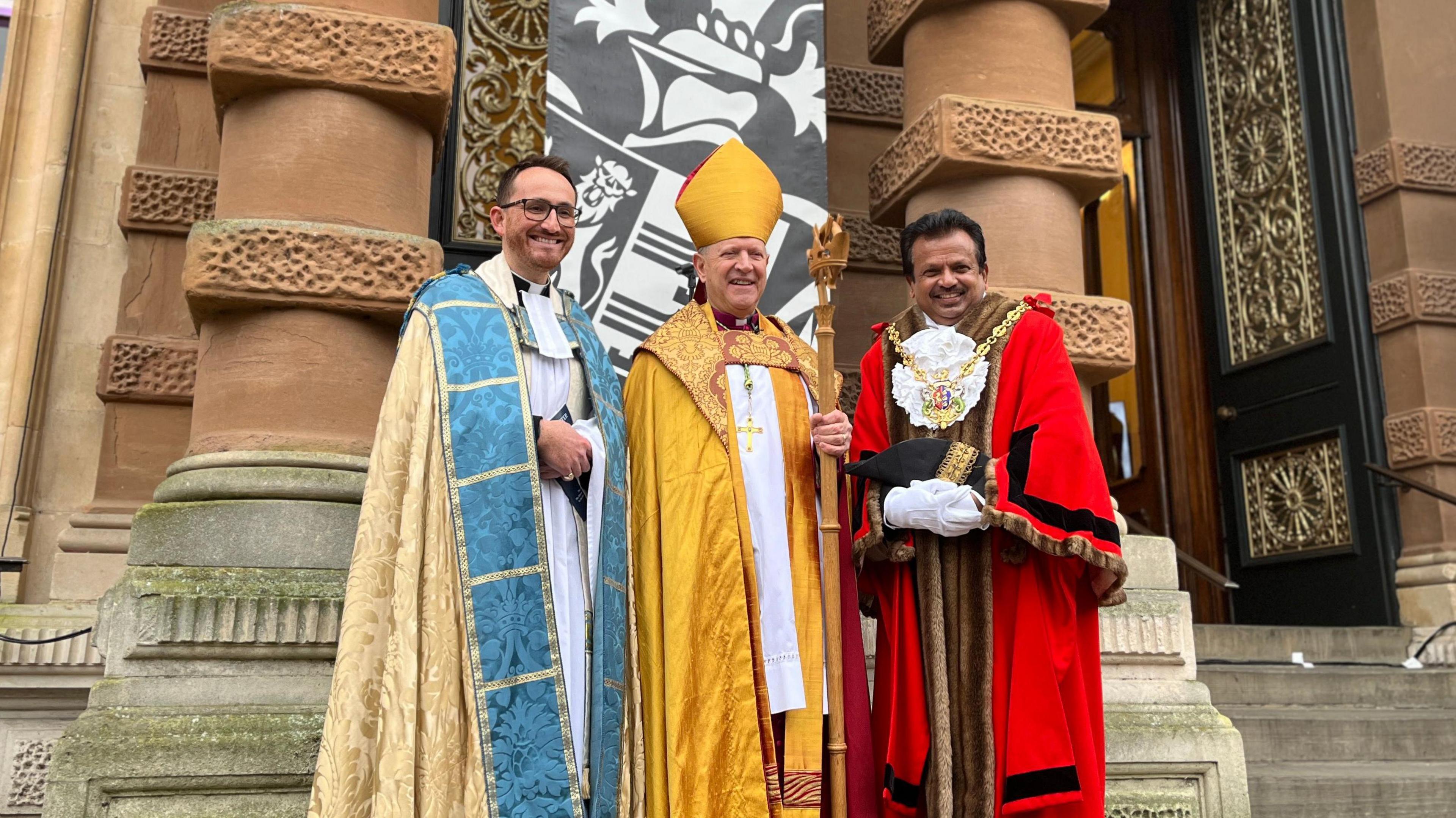 Vicar Tom Mumford, The Right Reverend Martin Seeley, and Ipswich mayor Elango K. Elavalakan, standing on the steps outside a building. They are all wearing various regalia and smiling at the camera.