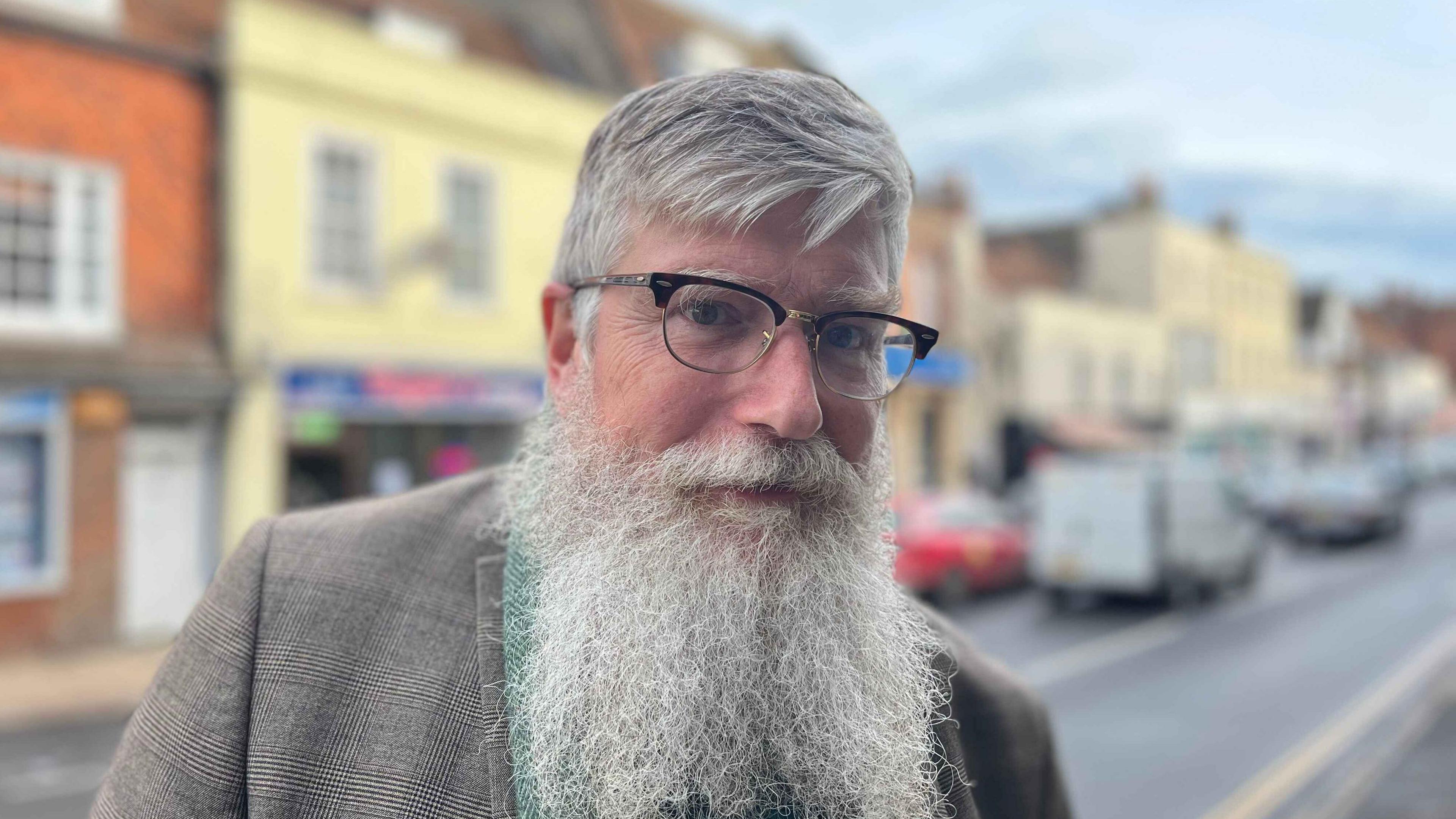 Philip Ardagh standing in the high street. He has grey hair and a big grey beard and glasses