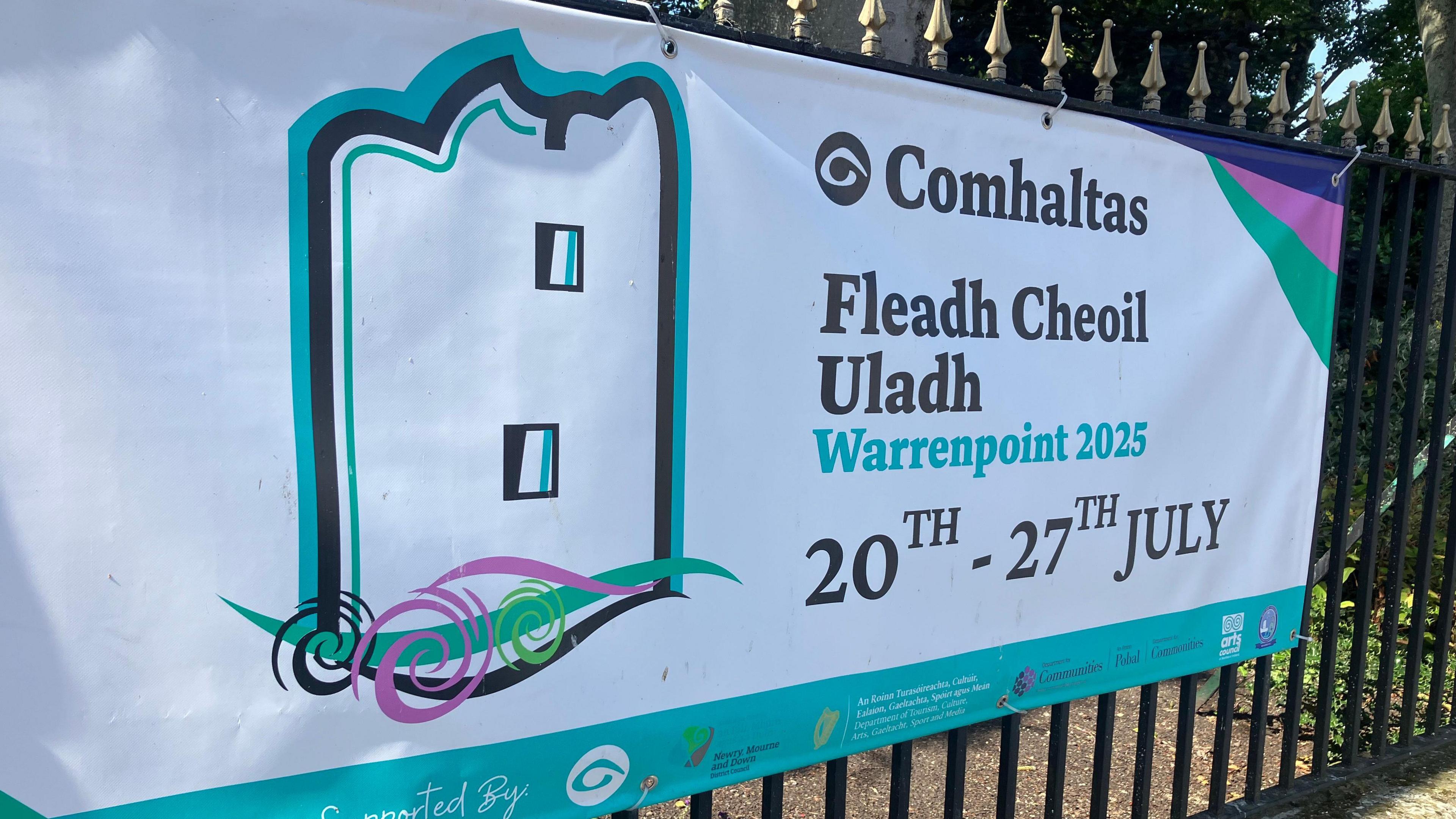A sign which says Comhaltas, Fleadh Cheoil Uladh, Warrenpoint 20th to 27th July is tied to railings.