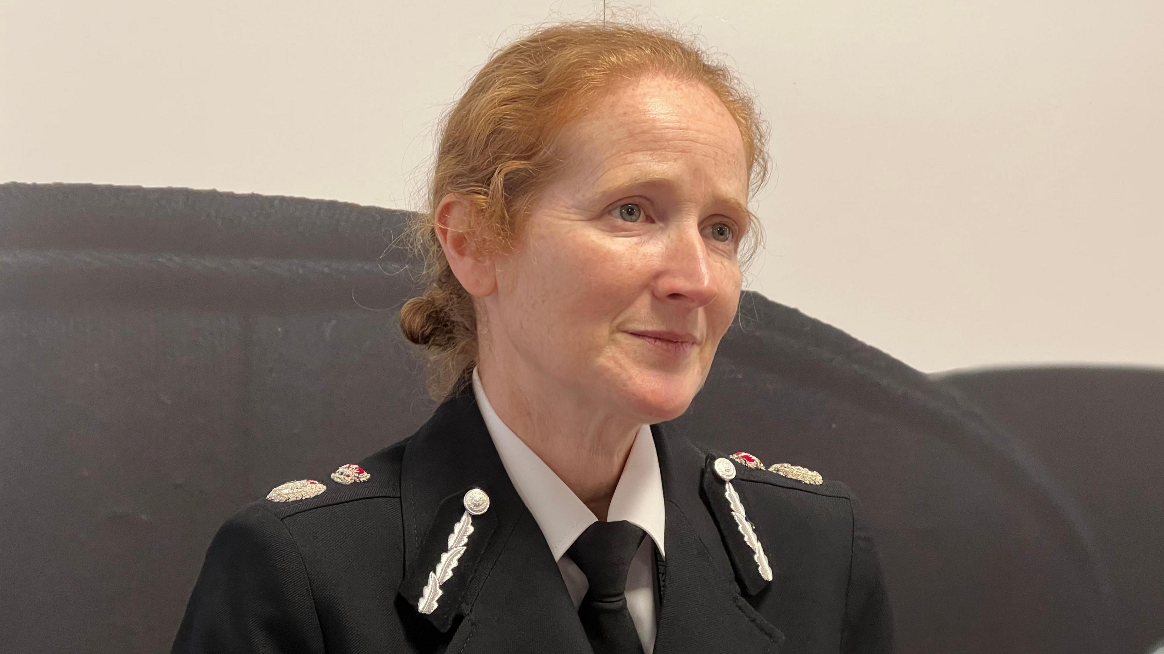 Catherine Roper pictured in uniform wearing a black jacket with silver and red embellishments on the collar and shoulder. She is looking away from the camera, and has red hair tied back in a low bun. 