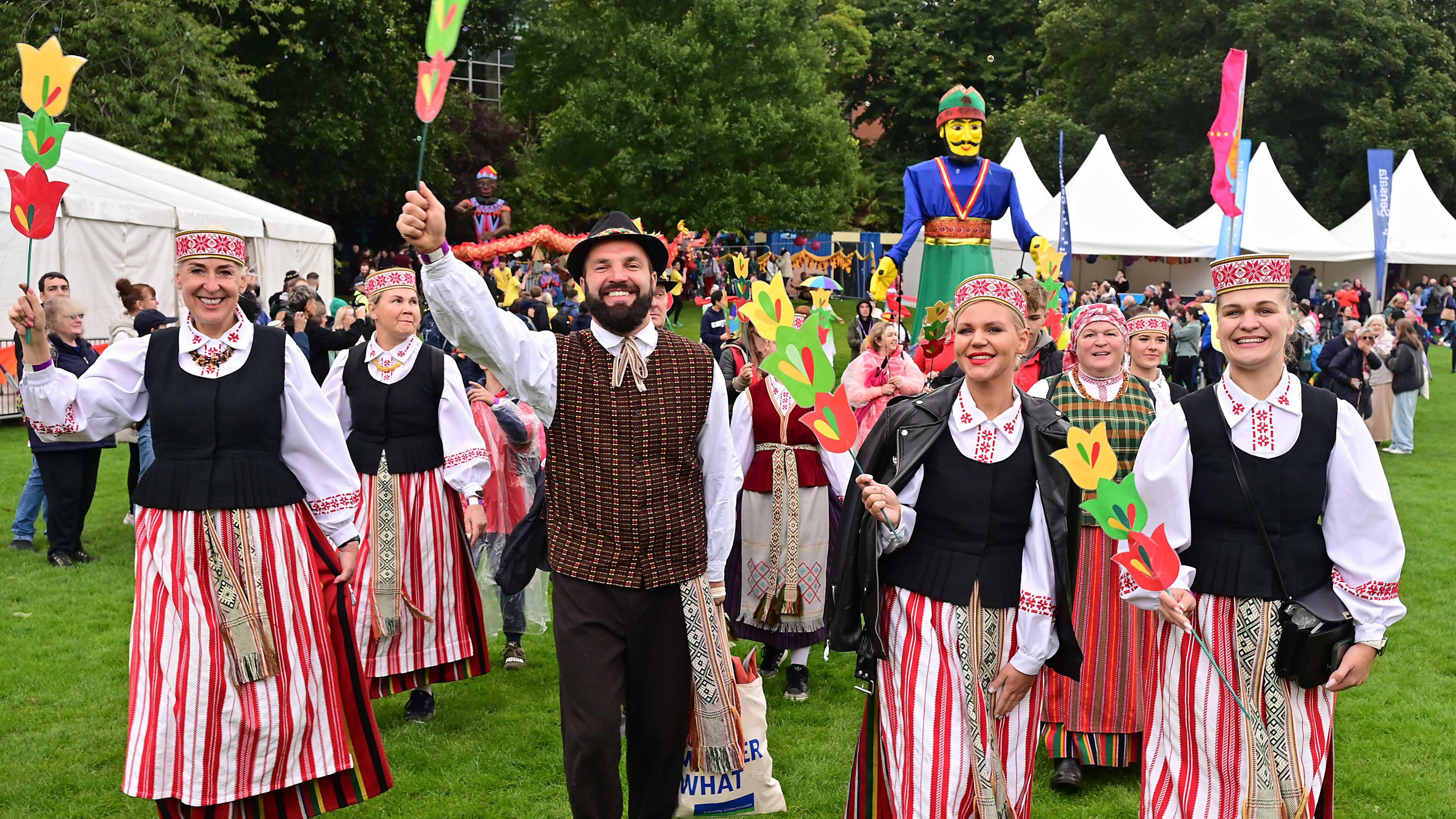 Group of people standing in traditional clothing with white festival tents behind them. 