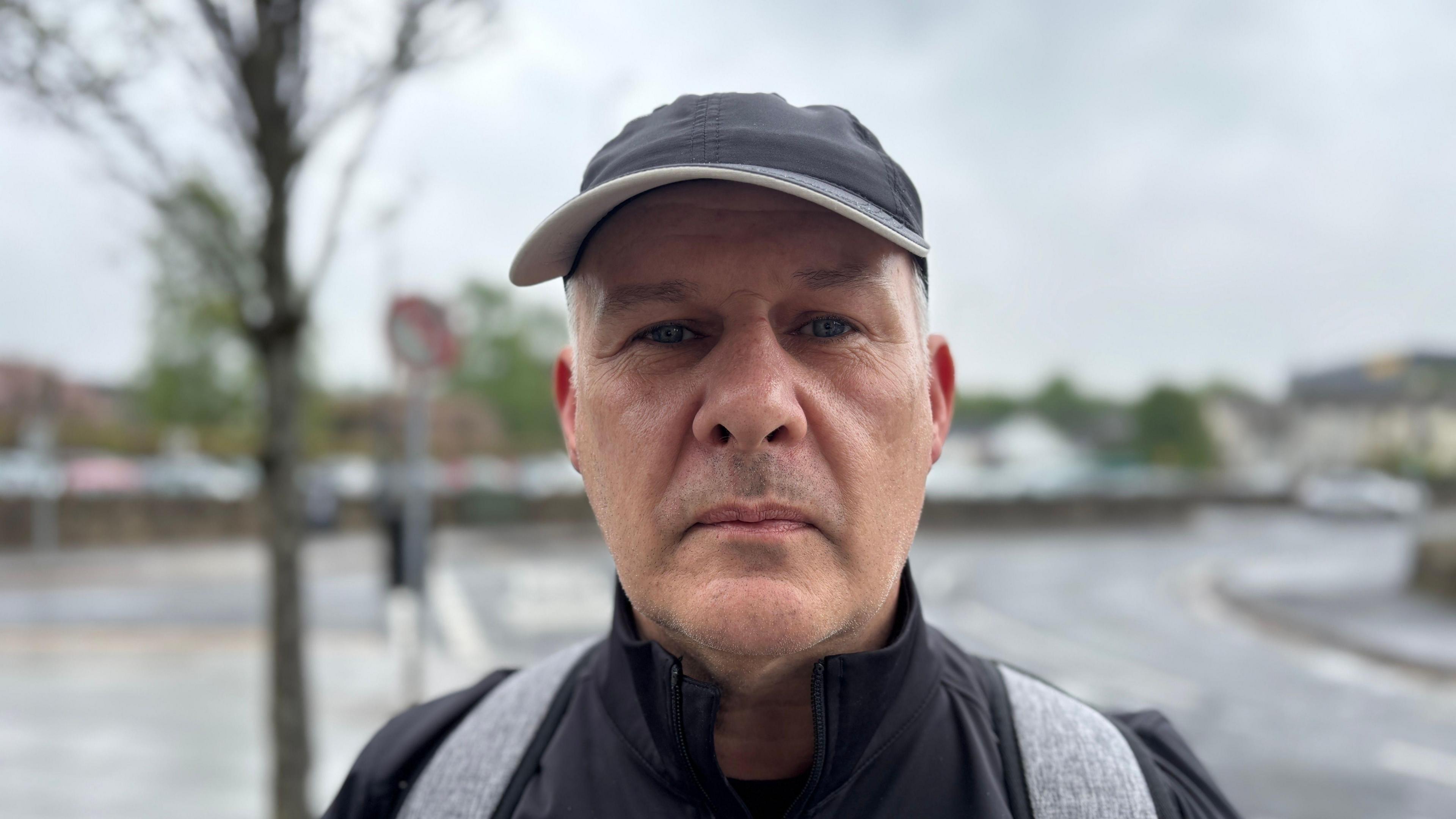 Billy Naylor. He is wearing a black cap, a black jacket and carrying a grey backback.
