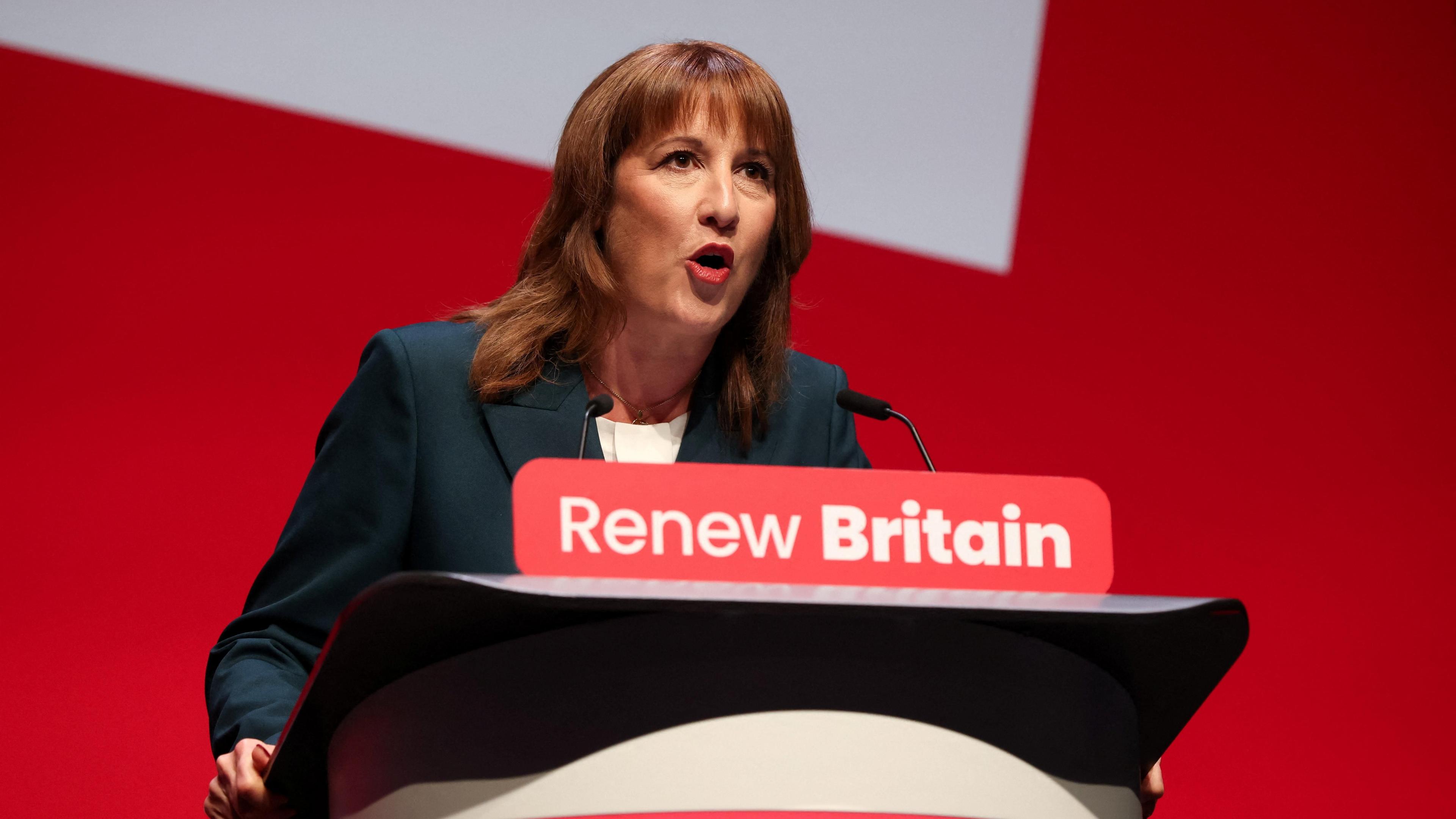 Rachel Reeves speaking from behind a lectern with a banner reading "Renew Britain" in front of a red and white-painted wall.