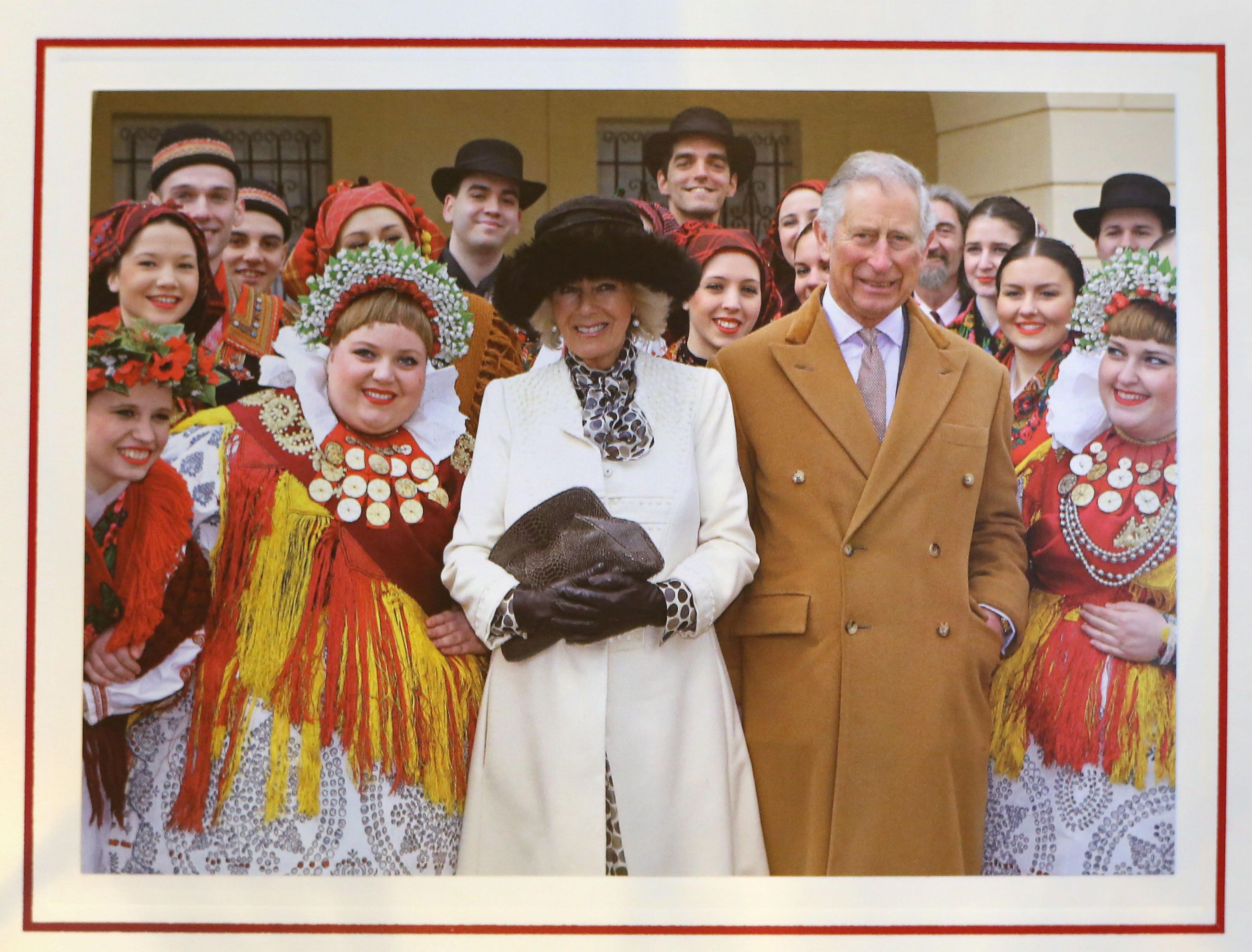 Prince Charles and Camilla's 2016 card, showing the couple during a visit to Croatia, standing in winter coats - Camilla with warm hat and gloves, Charles with his hands in his pockets. Performers dressed in costumes are standing either side of the royal couple and behind them.