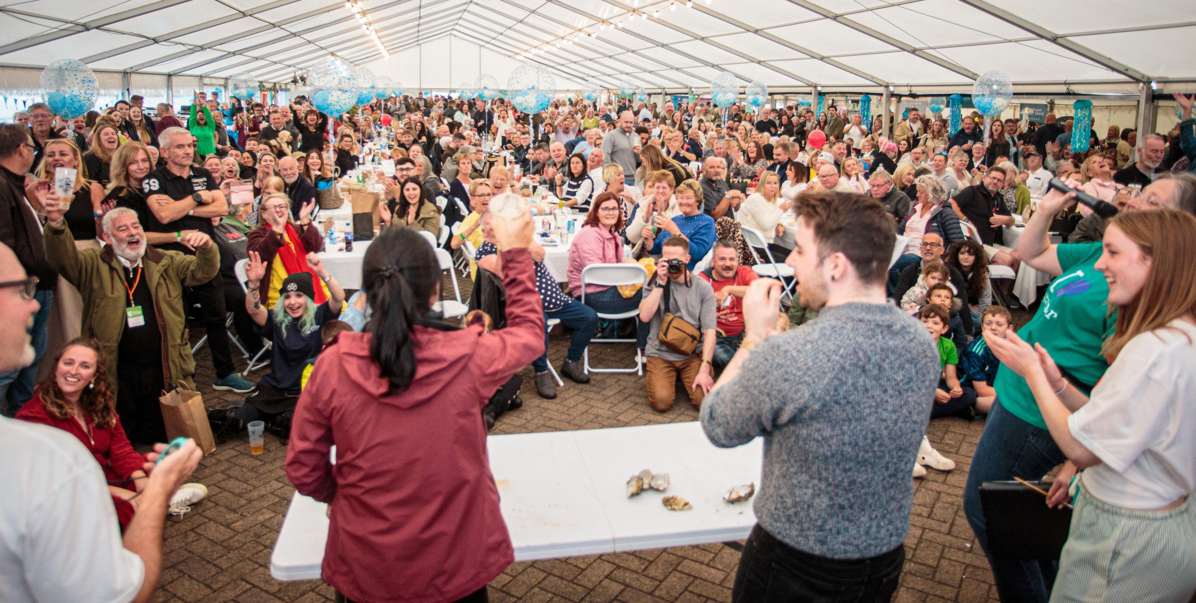 A large crowd of people at an oyster tasting event viewed from behind the people giving the presentation