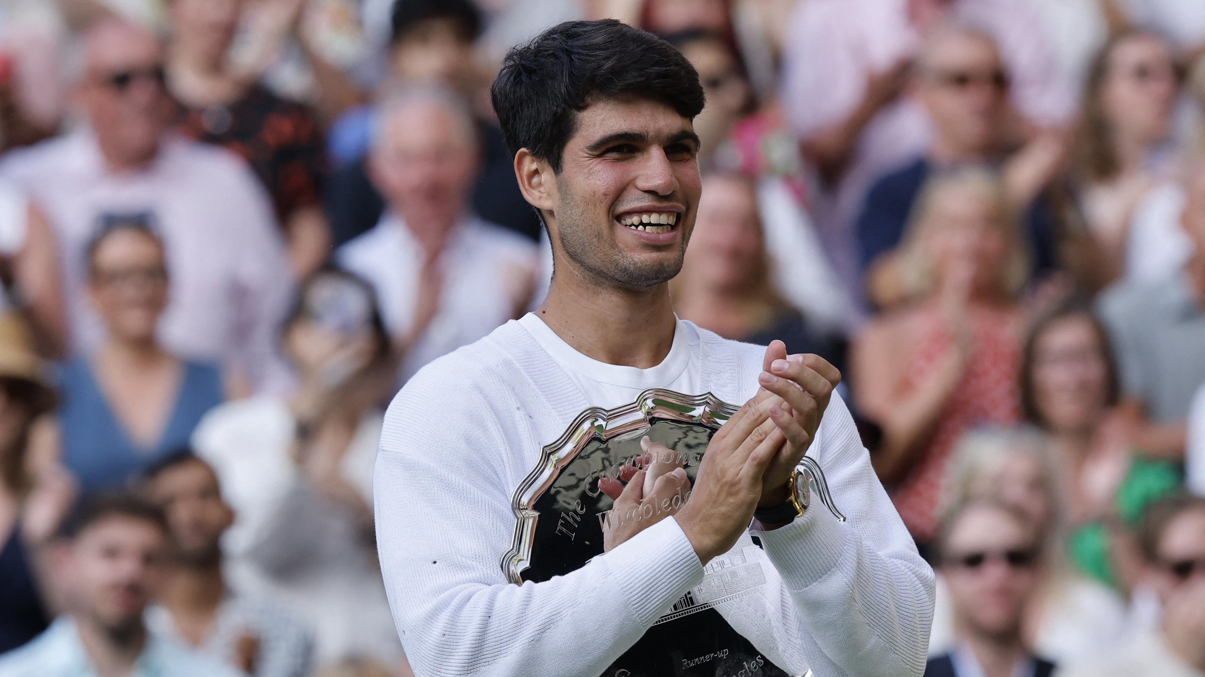 Carlos Alcaraz smiles and applauds while holding runner-up trophy at Wimbledon on Centre Court
