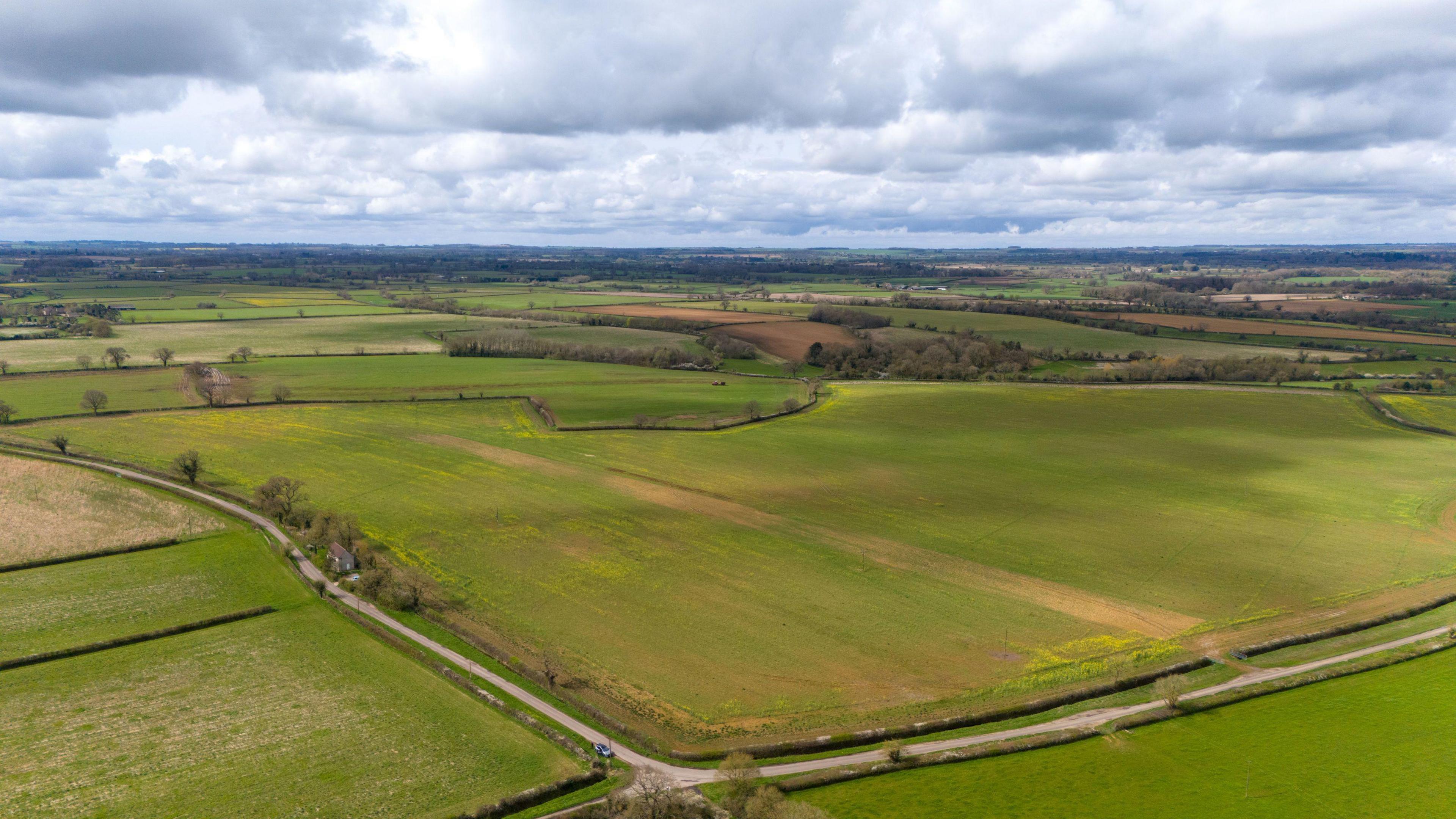 A drone shot of green fields going into the distance, two small country lanes within them there