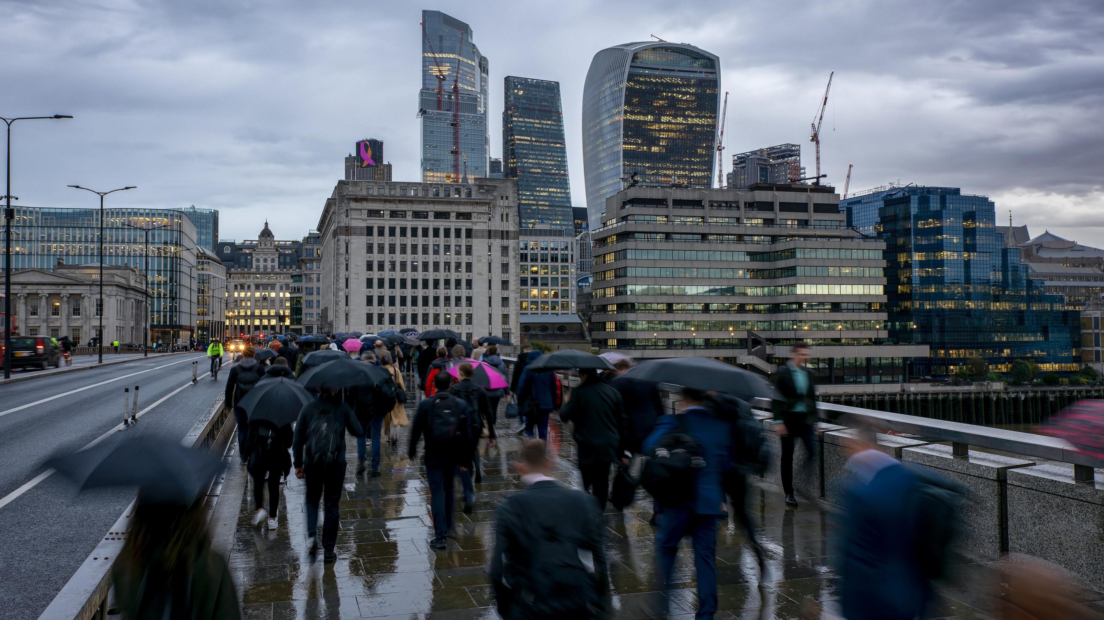 Blurred motion view of commuters with umbrellas in London going to work on a rainy, gray day in front of the city skyline during morning rush hour