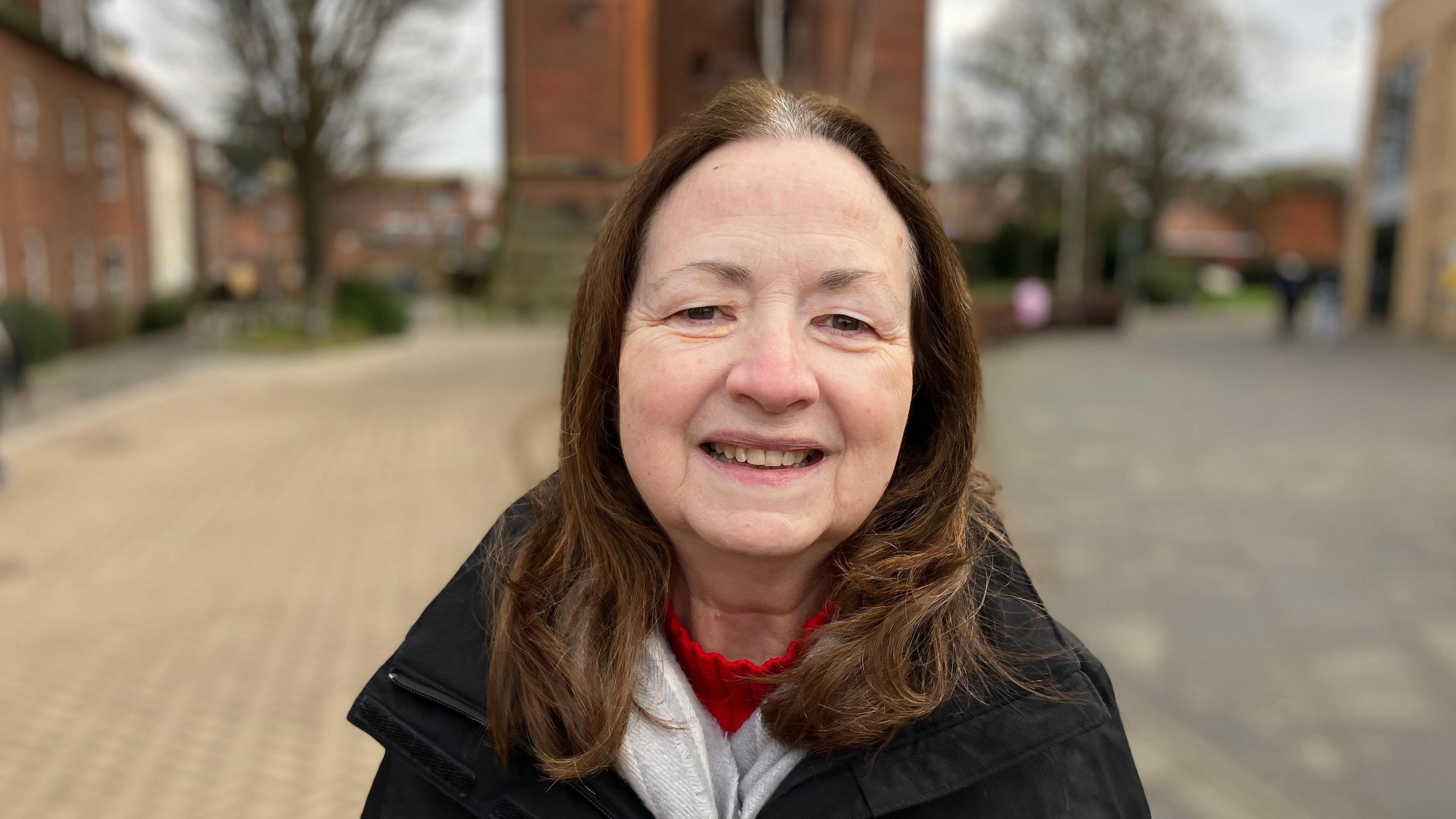 A woman with dark, medium length hair smiles at the camera with a blurred water tower in the background