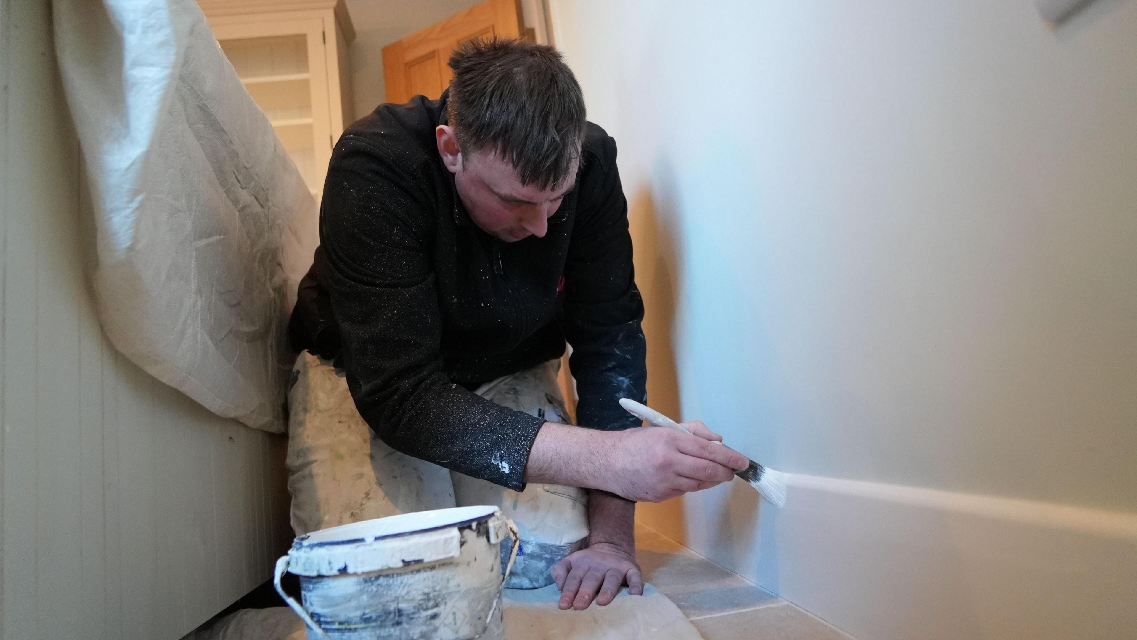 Picture of bowler Wayne Willgress on his hands and knees painting the skirting board in a house. He said he enjoys his job as a decorator as it gives him the flexibility he needs to play bowls semi-professionally