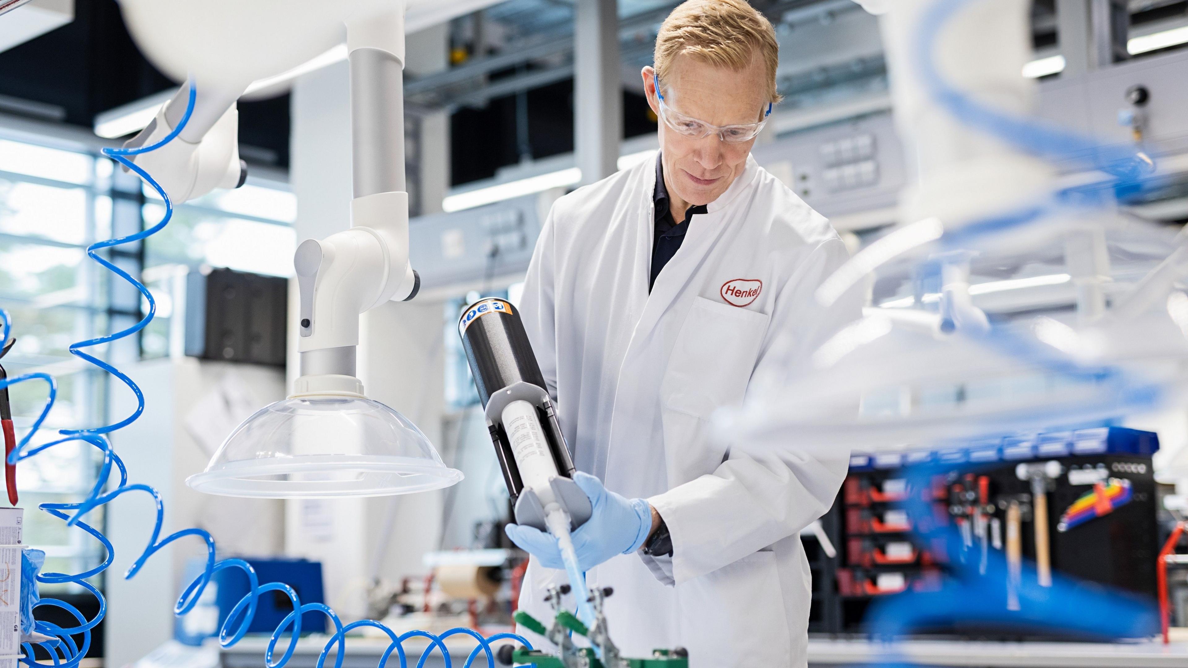 A Henkel scientist in a white lab coat uses equipment to dispense adhesive