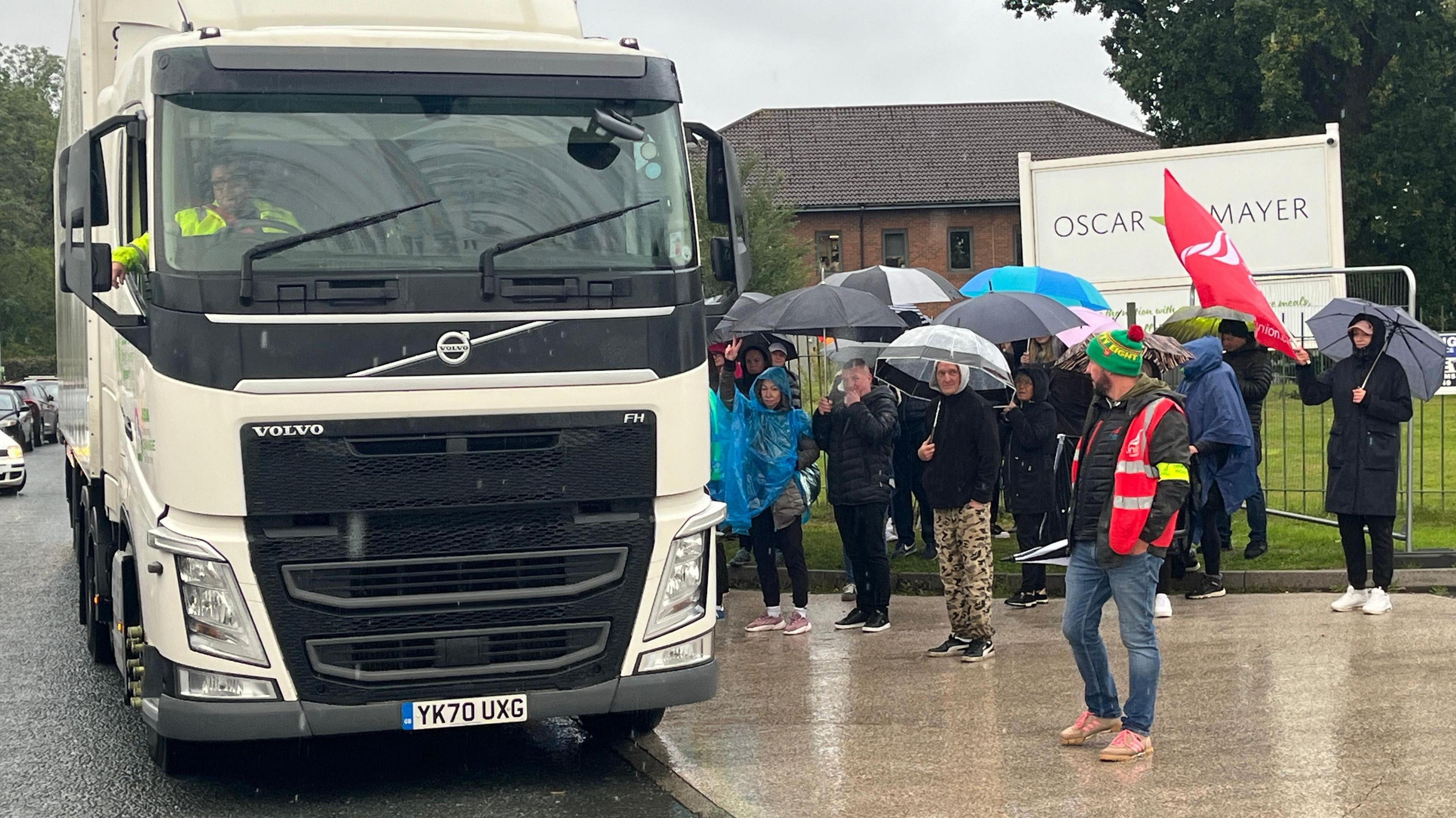 Striking workers stand next to a delivery lorry outside the factory