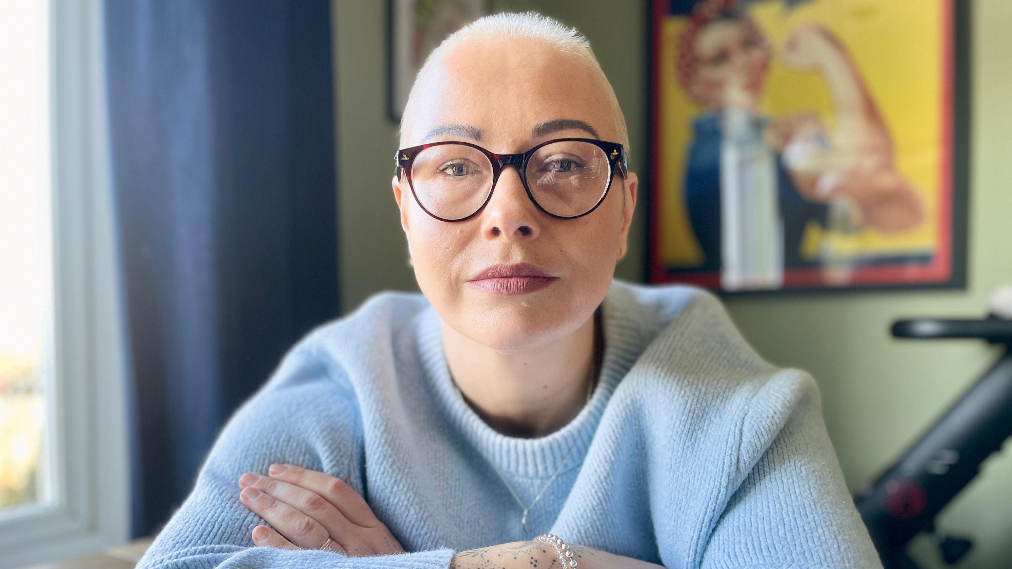 Close up of Jules Fielder wearing glasses and a blue jumper looking to camera